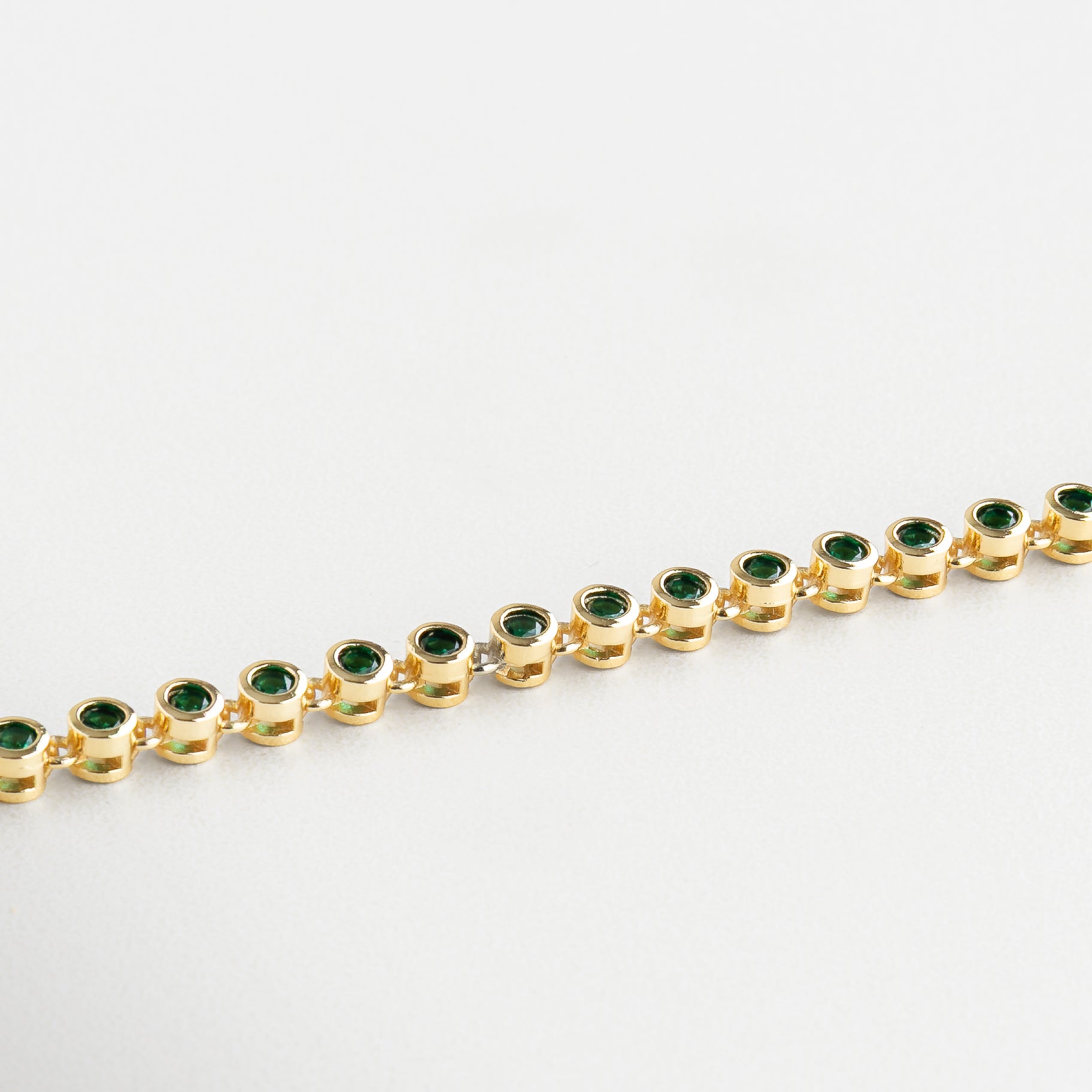 Detalle de zirconias verdes en pulsera dorada, Primer plano de pulsera con incrustaciones verdes, Zirconias cúbicas verdes sobre chapa de oro 18K, Acabado brillante en pulsera con piedras verdes