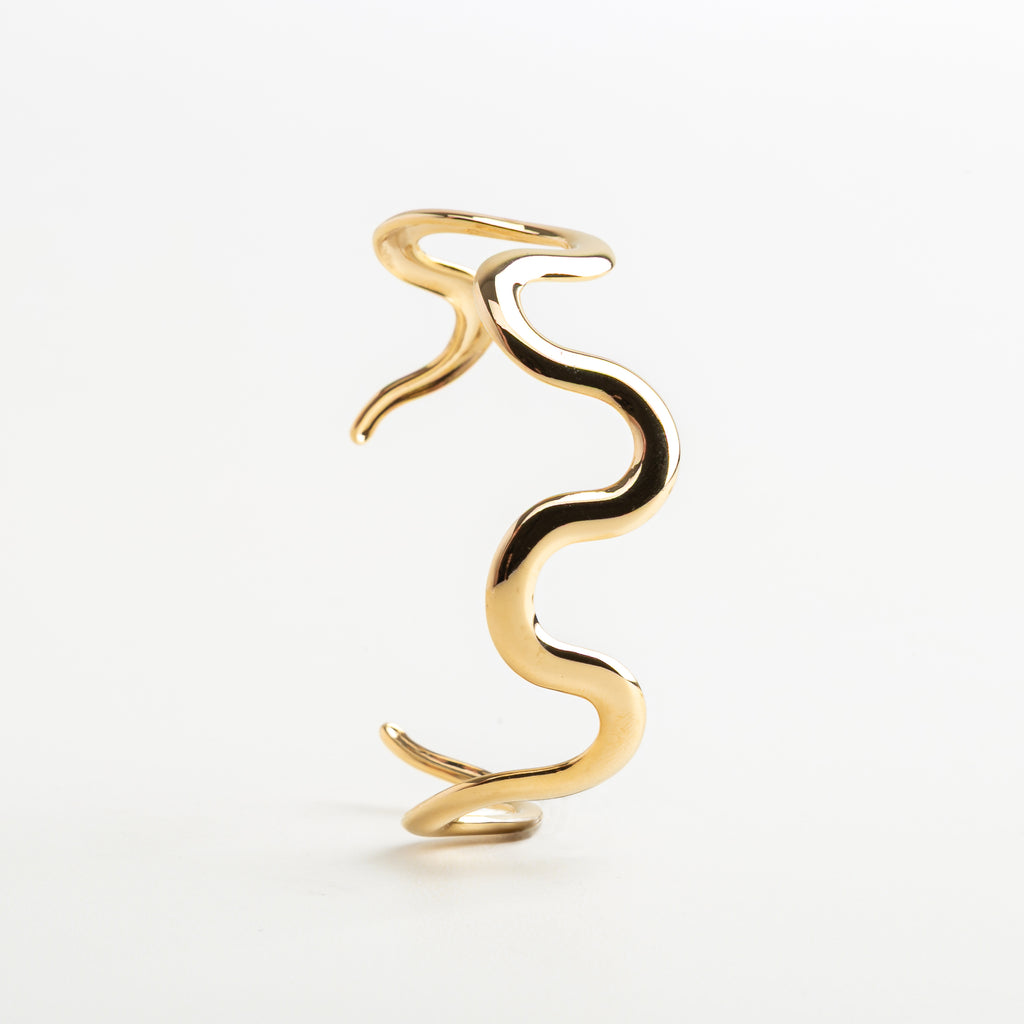 Pulsera tipo brazalete con forma fluida en dorado, Diseño ondulado dorado en acero inoxidable, Pulsera moderna de líneas fluidas y estilo elegante, Detalle del movimiento en pulsera Maya dorada