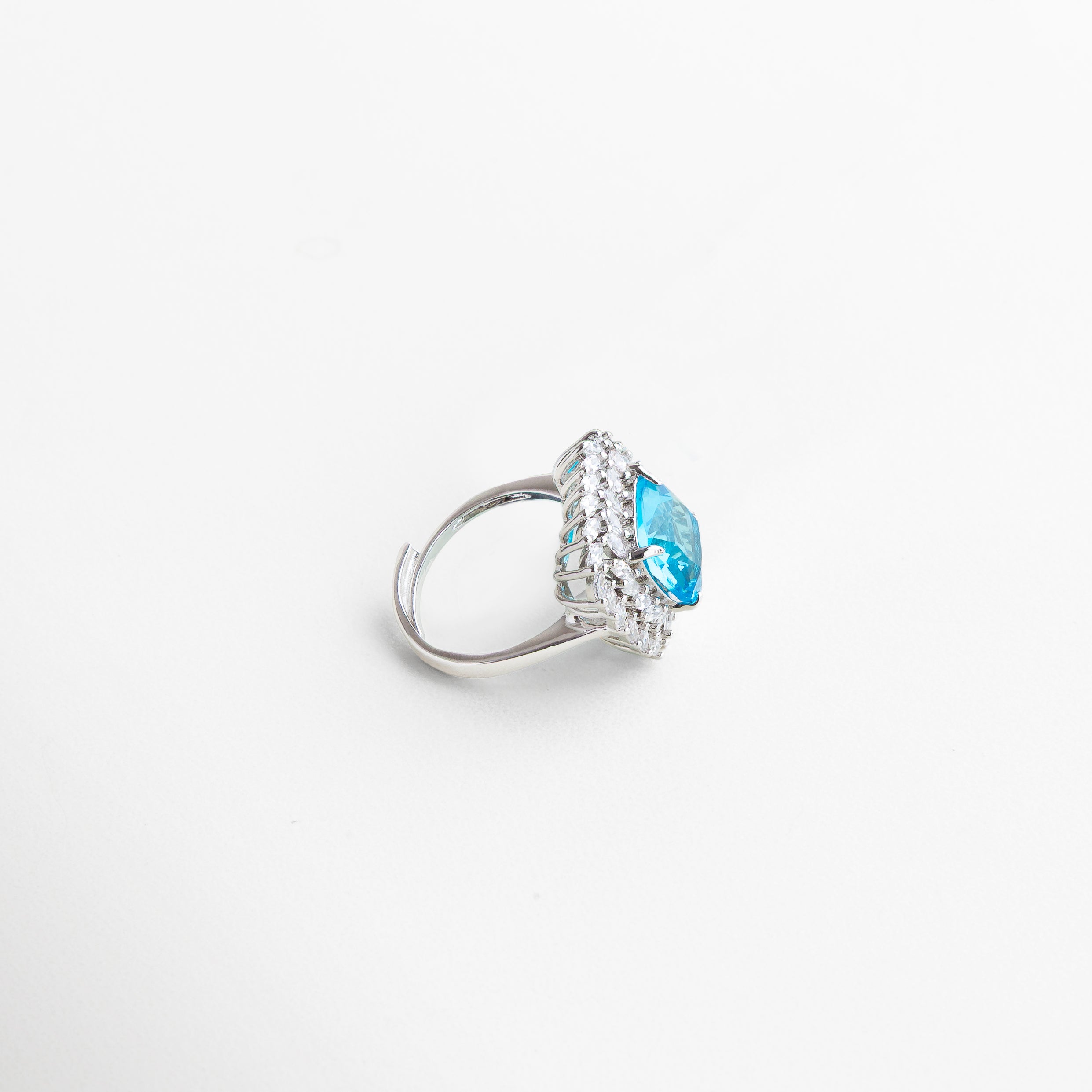 Anillo Lanikai Aqua visto de perfil, con borde plateado y piedra azul elevada que capta la luz con cada ángulo. Vista lateral del anillo con centro azul, mostrando su estructura delicada y brillo sofisticado. Perfil del anillo Lanikai Aqua, destacando el volumen de la zirconia azul y el contraste con el metal plateado. Detalle lateral del anillo con piedra azul, ideal para looks glamorosos y ocasiones especiales. Anillo Lanikai Aqua visto desde el lado, con diseño moderno y piedra central qu