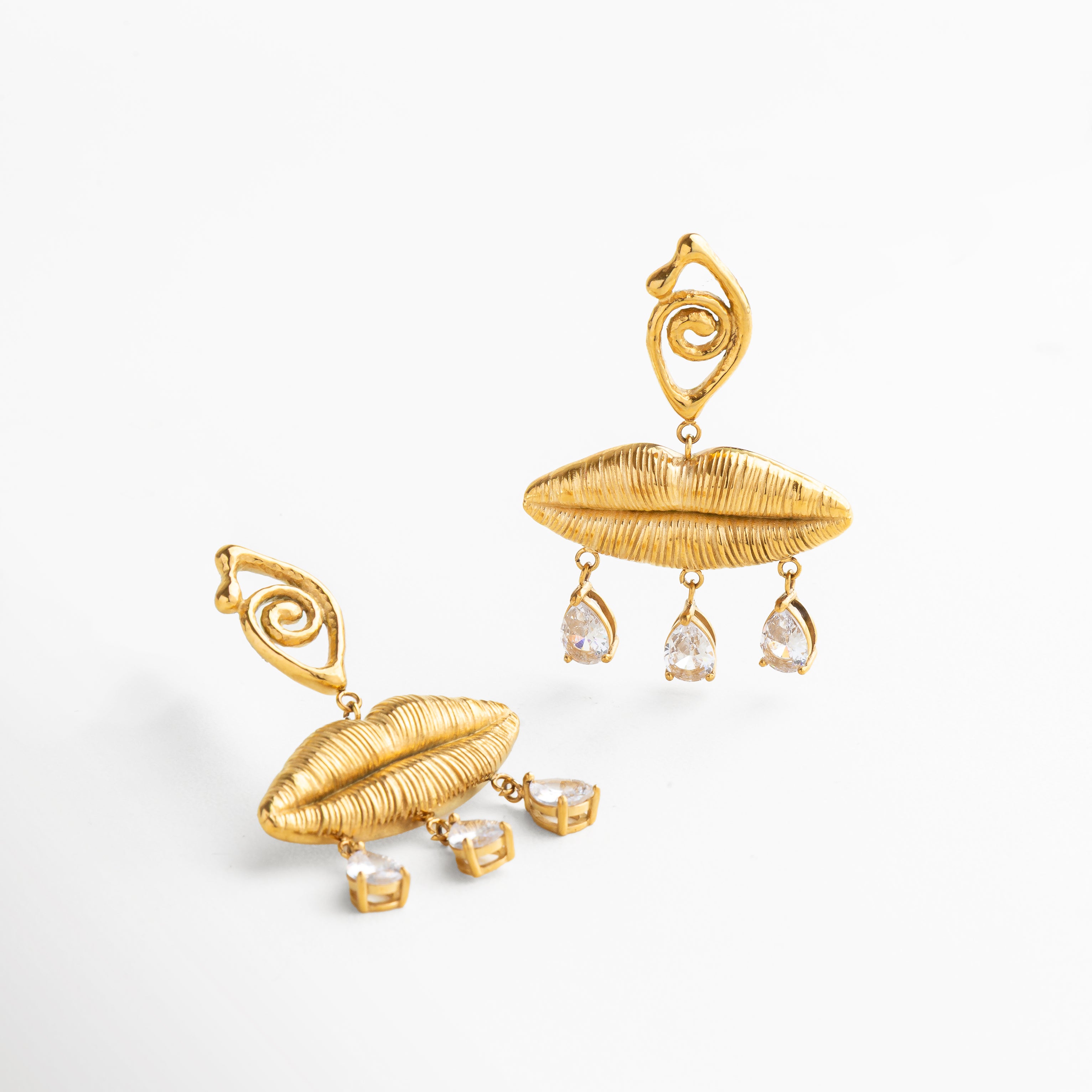 Primer plano de labios dorados con textura definida, Detalle de engaste de zirconias brillantes en colgante, Acabado pulido con relieve artístico en la parte superior, Brillo intenso del recubrimiento en oro 18K, Contraste entre textura metálica y destellos de zirconias