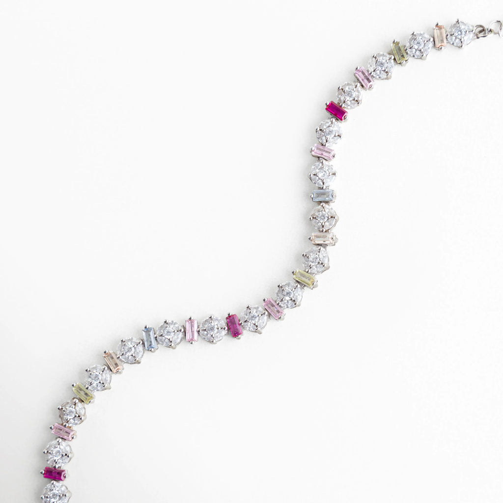 Pulsera flexible de plata 925 con diseño de piedras multicolor en forma de S, Brazalete plateado con circonias de colores mostrando su caída y movimiento natural, Pulsera de oro blanco y plata con cristales brillantes dispuestos en hilera curva, Diseño de joyería artesanal: pulsera "Rainbow" plateada con piedras de diferentes formas, Pulsera delgada de plata con destellos multicolores, ideal para un look juvenil y elegante.