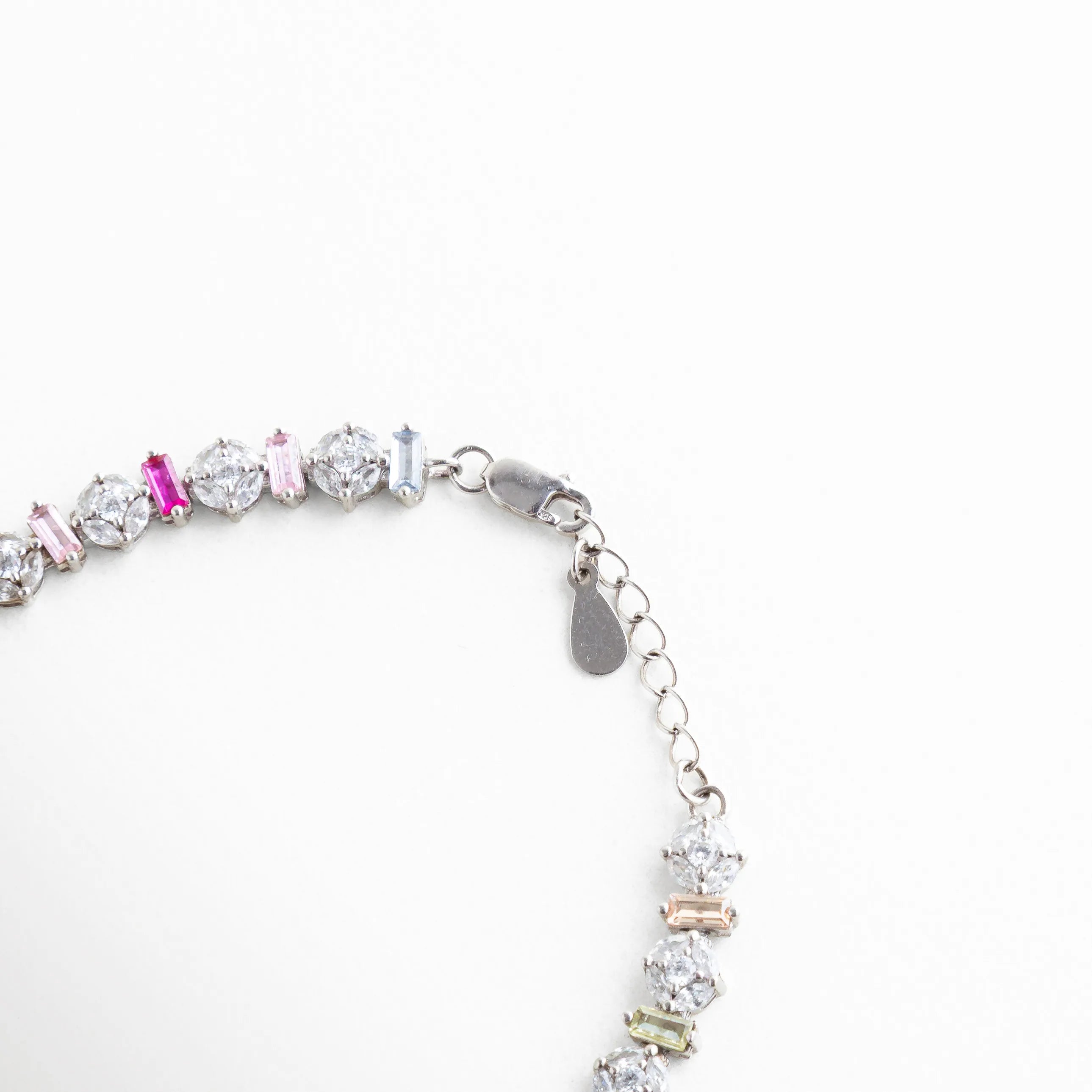 Detalle del broche de langosta y cadena de extensión en pulsera de plata 925, Vista técnica del cierre seguro y acabado en oro blanco de pulsera multicolor, Broche ajustable de joyería en plata con placa de autenticidad "925", Detalle de la cadena ajustable para diferentes medidas de muñeca en pulsera dorada blanca, Mecanismo de cierre de pulsera de circonias resaltando la calidad del metal.