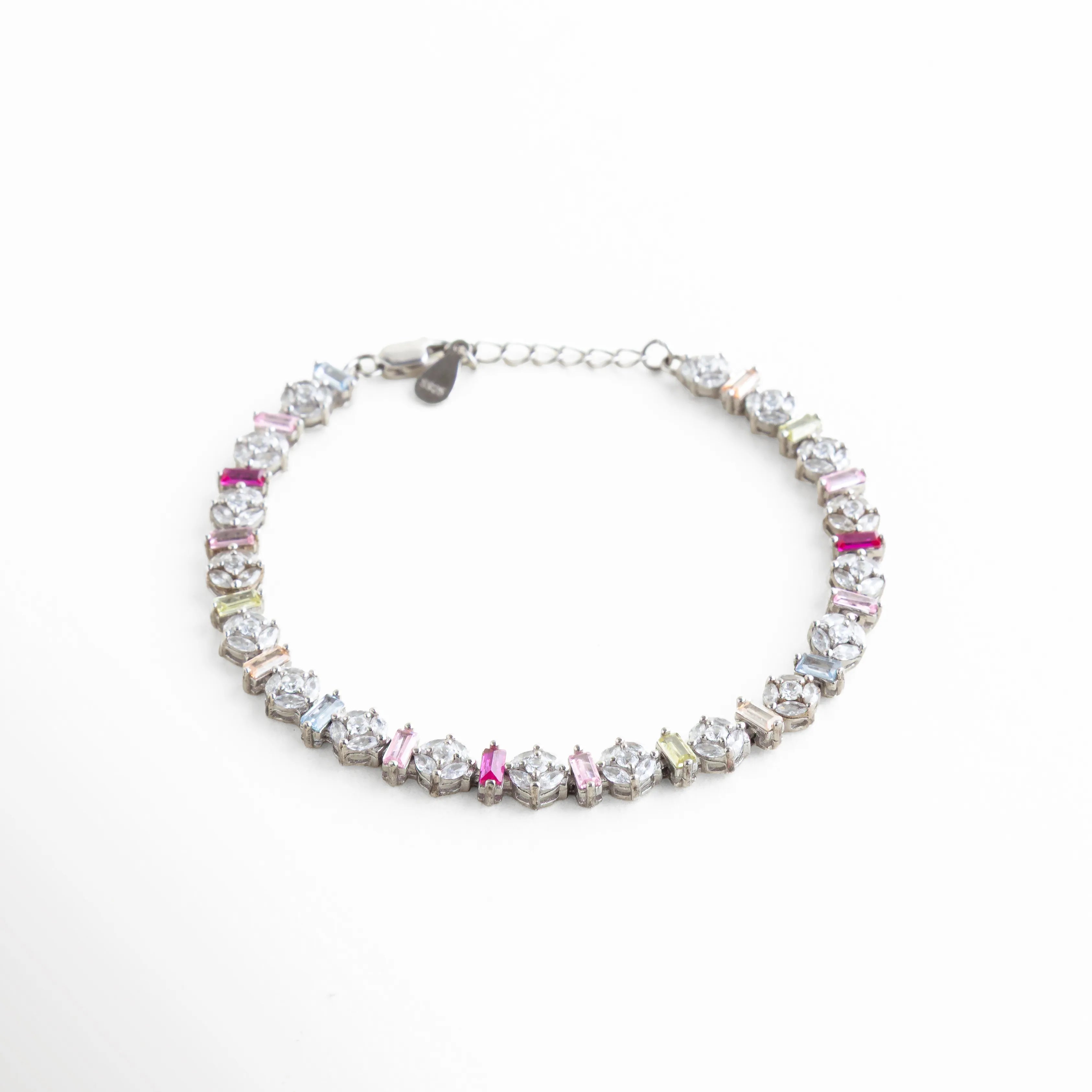 Perspectiva angular de pulsera de plata resaltando el brillo de las circonias bajo la luz, Pulsera de lujo accesible en oro blanco con piedras de colores, vista de 45 grados, Brazalete brillante de plata ley 925 con diseño "Pastel Rainbow", Joyería de tendencia: pulsera delgada plateada con circonias de corte baguette y redondo, Vista lateral de pulsera multicolor mostrando el relieve y brillo de los cristales.