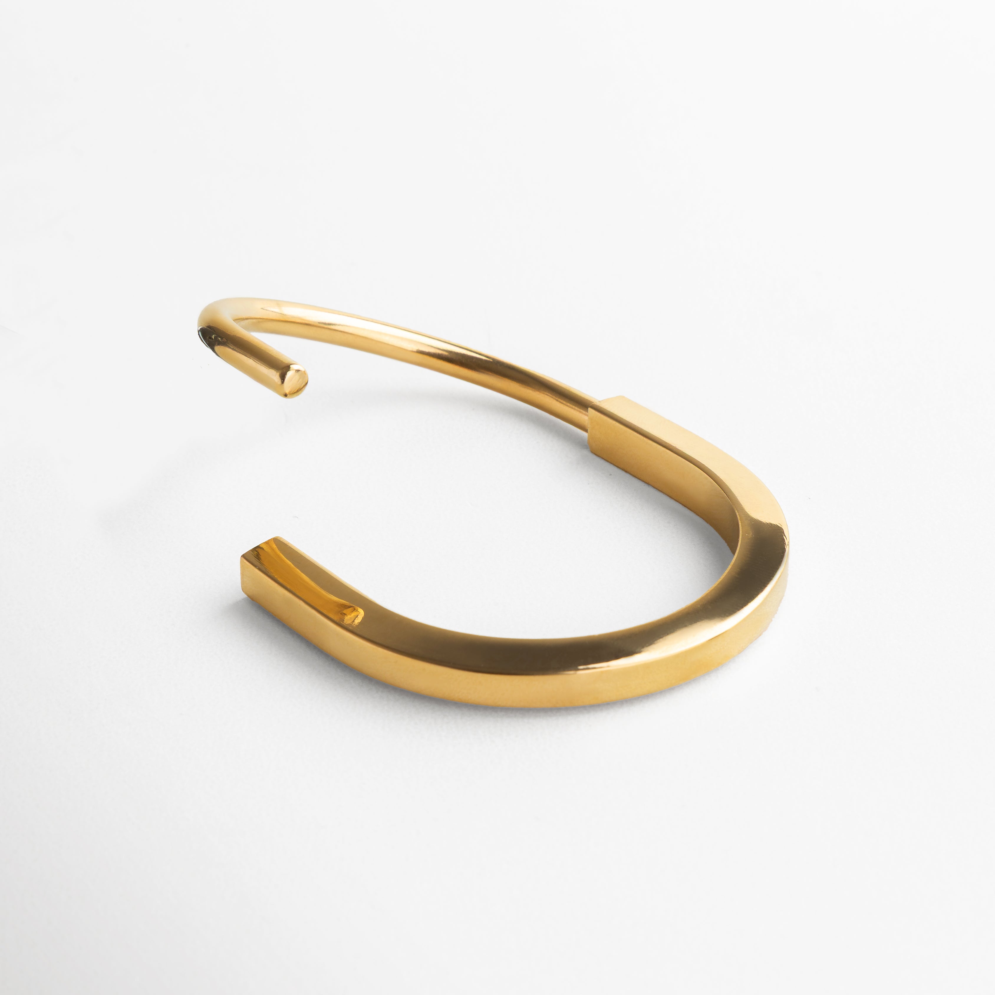 Material base de acero inoxidable que garantiza durabilidad y resistencia, Recubrimiento de alta calidad con baño en chapa de oro 18K para un acabado premium, Textura suave y pulida que refleja la luz sutilmente en cada movimiento, Bordes bien definidos que enfatizan el carácter estructurado del diseño, Acabado impecable que evita el desgaste con el uso frecuente.