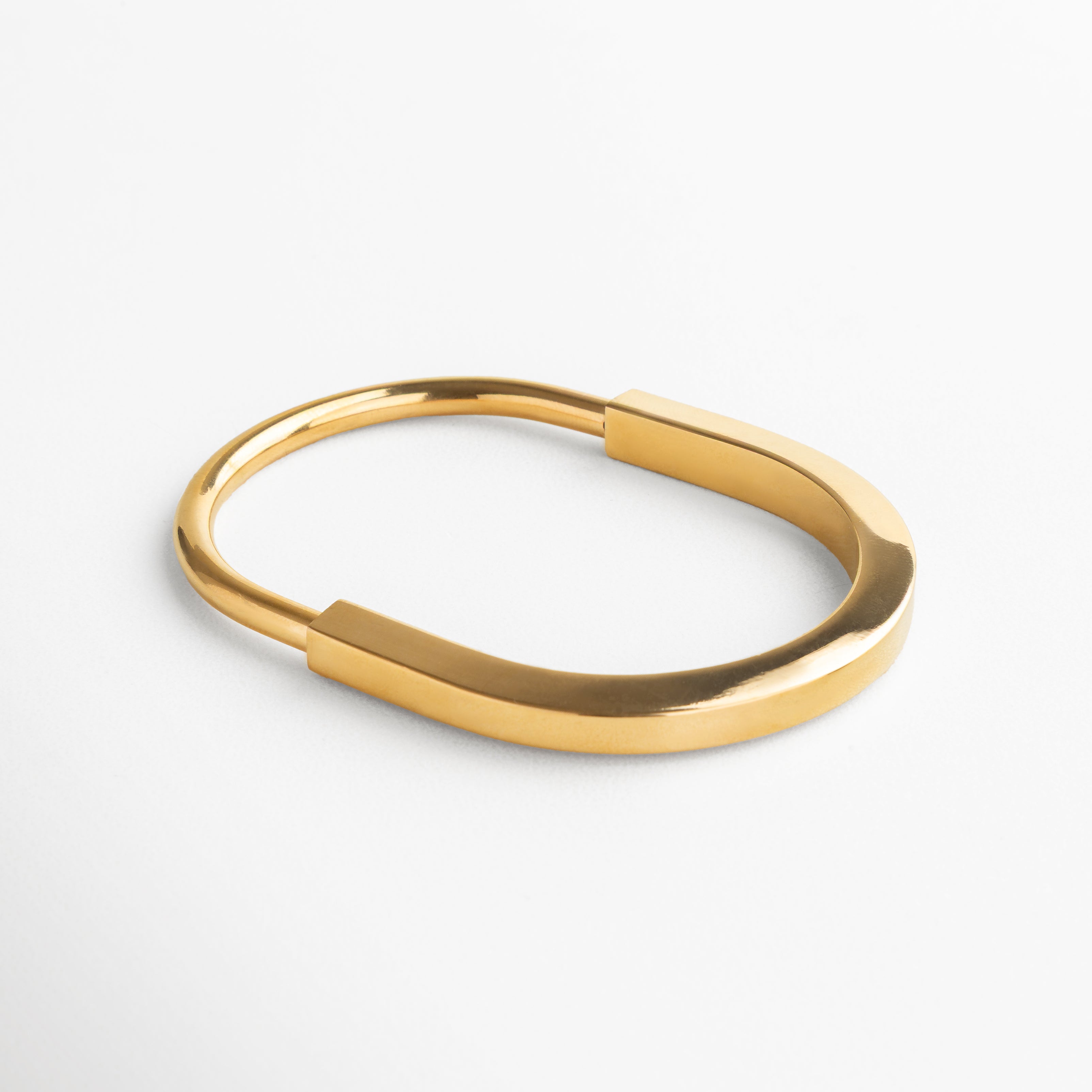 Pulsera dorada de acero inoxidable, Diseño estructurado y envolvente, Líneas limpias y definidas, Acabado brillante en baño de chapa de oro 18K, Forma ovalada para ajuste cómodo, Dimensiones: 7.3 cm largo, 5.8 cm ancho, Estilo moderno y sofisticado, ideal para outfits elegantes