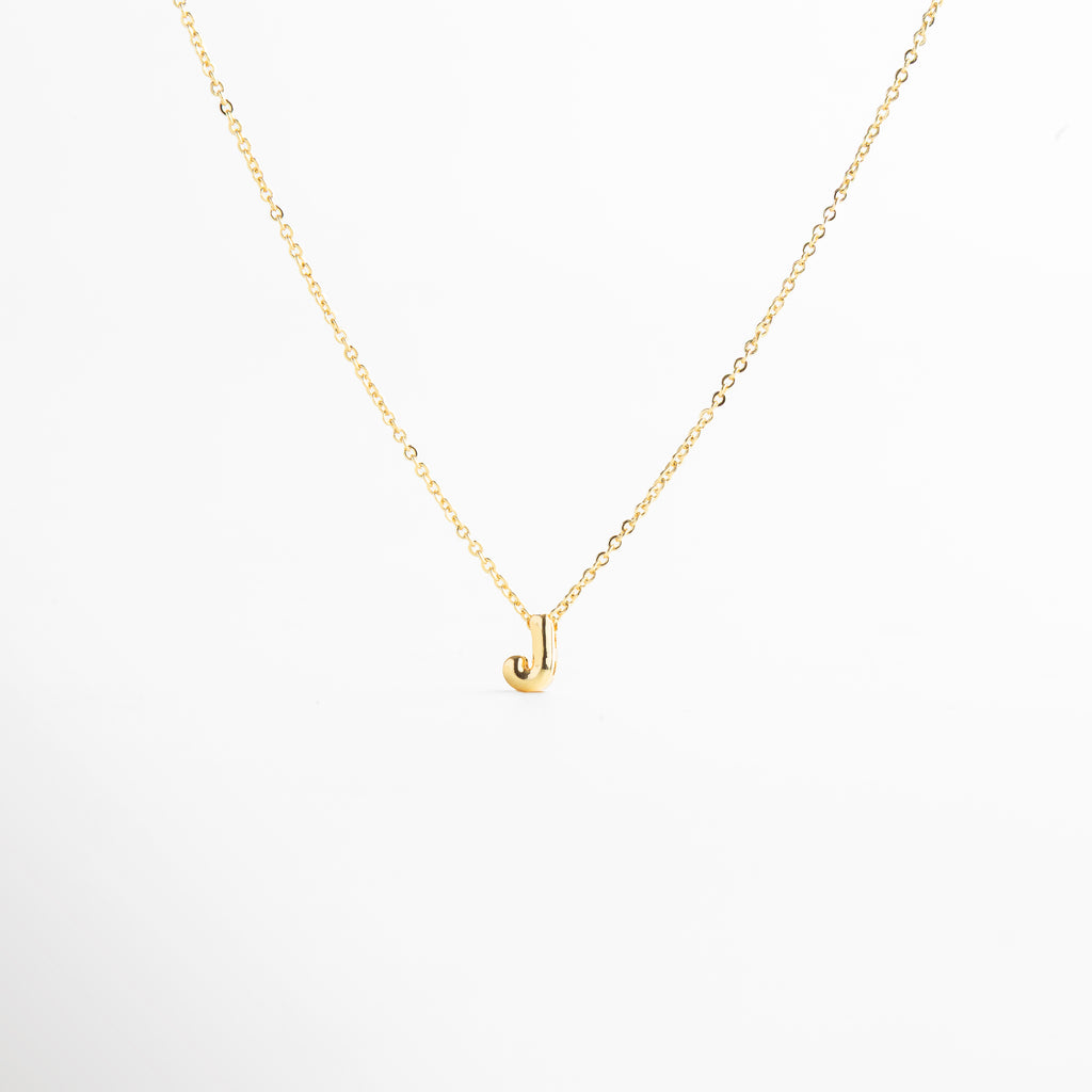 detalle de letra inicial J mini bold en collar dorado, textura del dije con inicial J chapada en oro, collar con inicial J vista de cerca, acabado brillante del collar con letra J, forma de la letra J en diseño mini bold