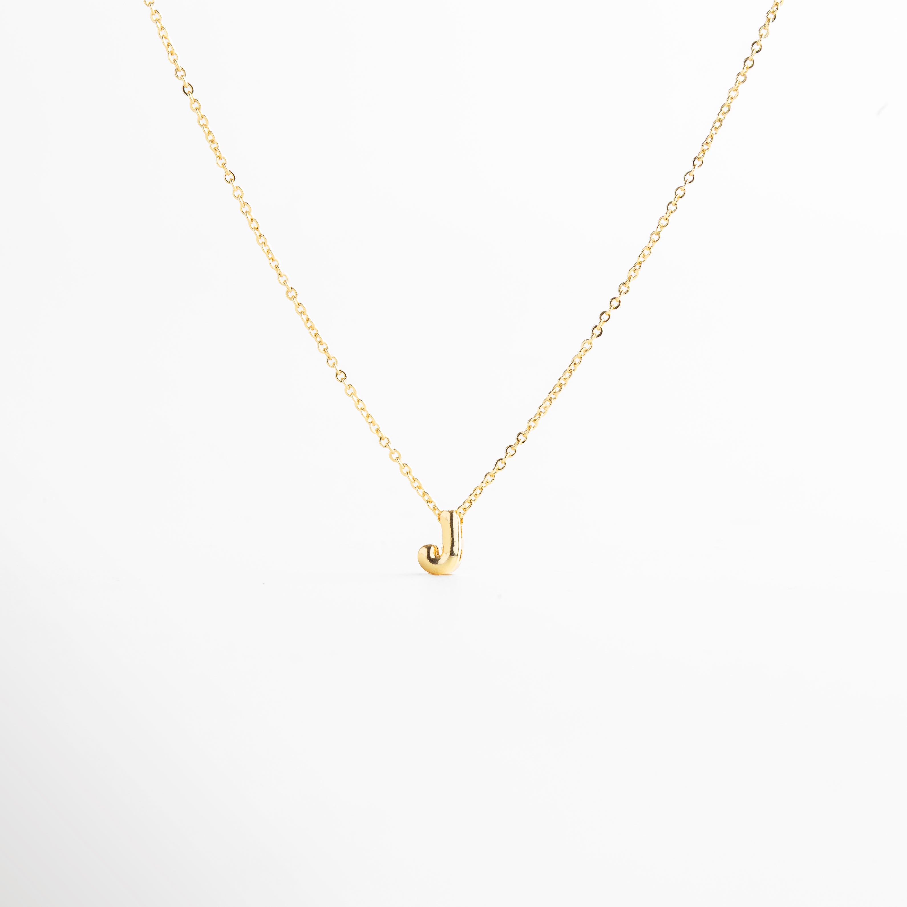 detalle de letra inicial J mini bold en collar dorado, textura del dije con inicial J chapada en oro, collar con inicial J vista de cerca, acabado brillante del collar con letra J, forma de la letra J en diseño mini bold