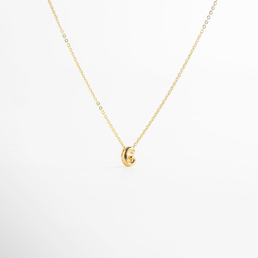 grosor del collar mini con inicial G dorada, detalle del diseño bold en la letra G del collar, cadena fina con dije de inicial G, acabado enchapado en oro 18K con letra G, collar de cobre con recubrimiento dorado