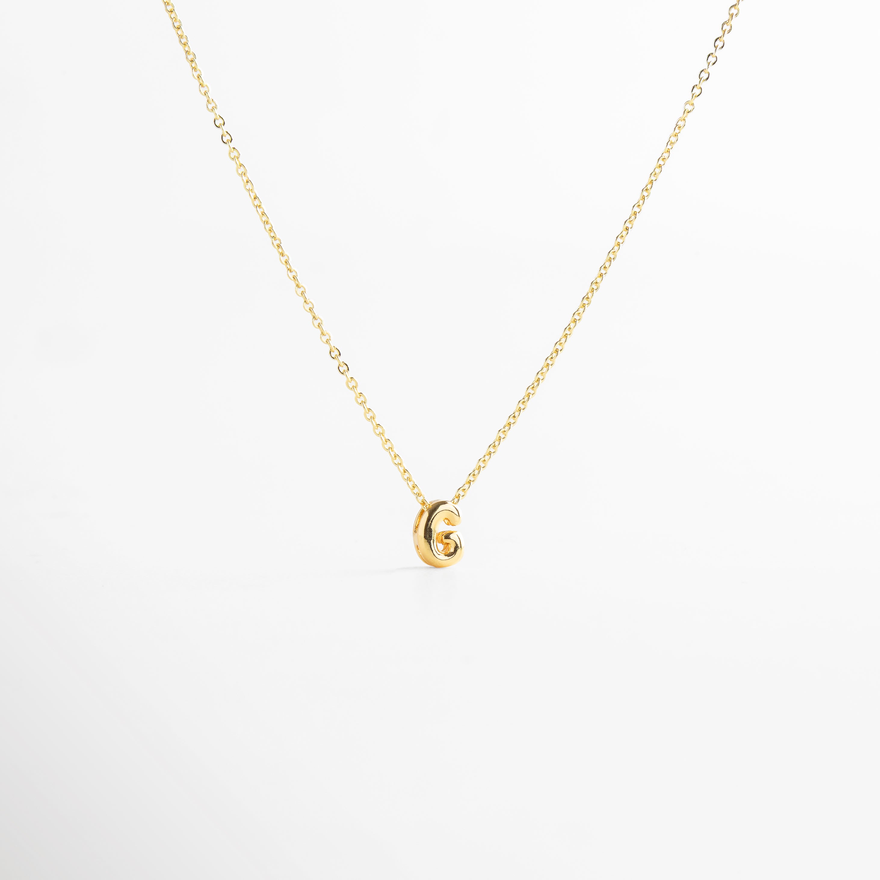 grosor del collar mini con inicial G dorada, detalle del diseño bold en la letra G del collar, cadena fina con dije de inicial G, acabado enchapado en oro 18K con letra G, collar de cobre con recubrimiento dorado