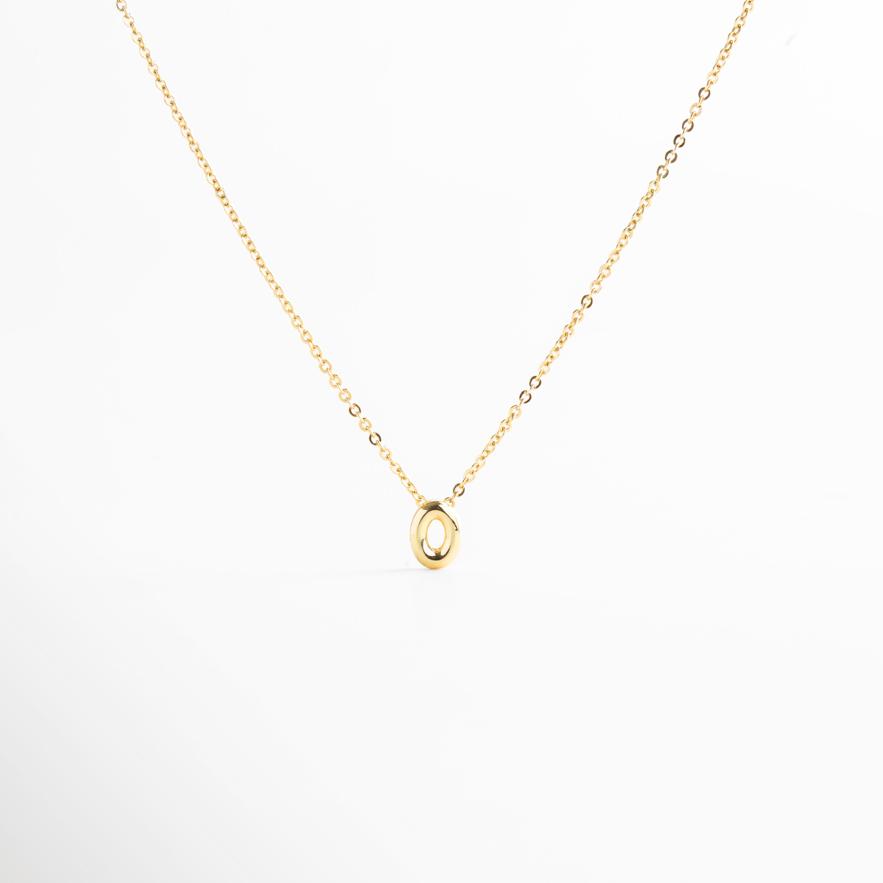 detalle de letra inicial O mini bold en collar dorado, textura del dije con inicial O chapada en oro, collar con inicial O vista de cerca, acabado brillante del collar con letra O, forma de la letra O en diseño mini bold