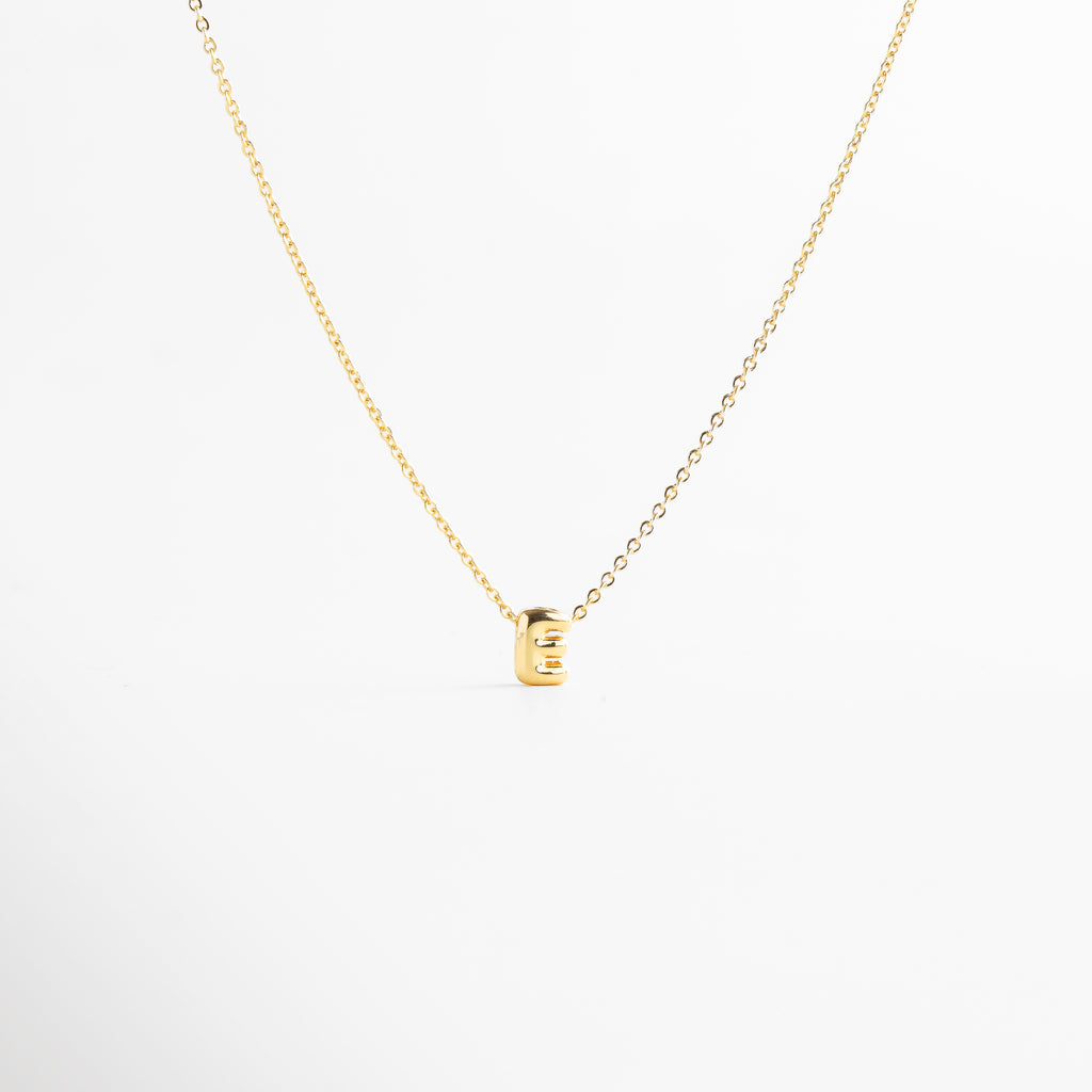 detalle de letra inicial E mini bold en collar dorado, textura del dije con inicial E chapada en oro, collar con inicial E vista de cerca, acabado brillante del collar con letra E, forma de la letra E en diseño mini bold