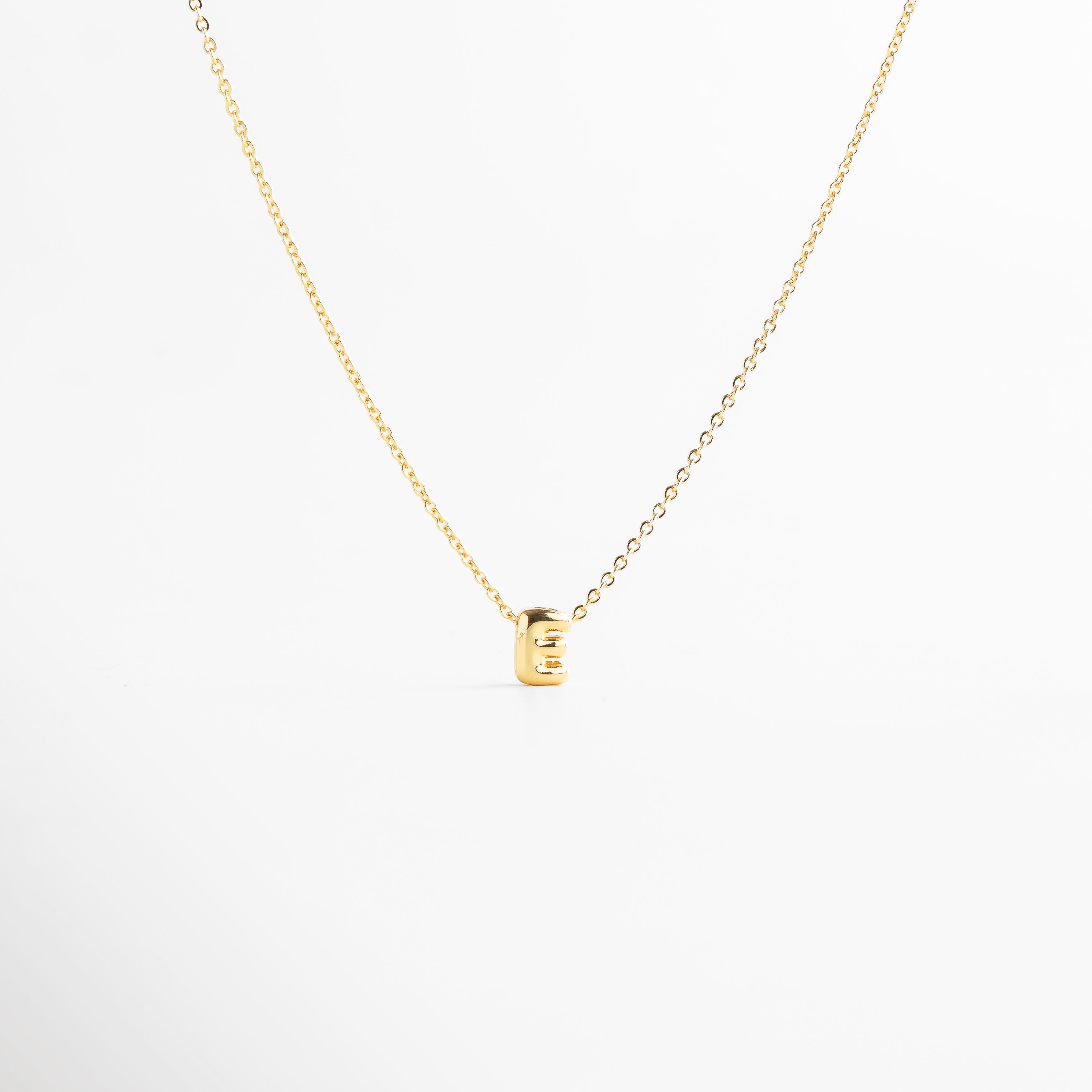 detalle de letra inicial E mini bold en collar dorado, textura del dije con inicial E chapada en oro, collar con inicial E vista de cerca, acabado brillante del collar con letra E, forma de la letra E en diseño mini bold