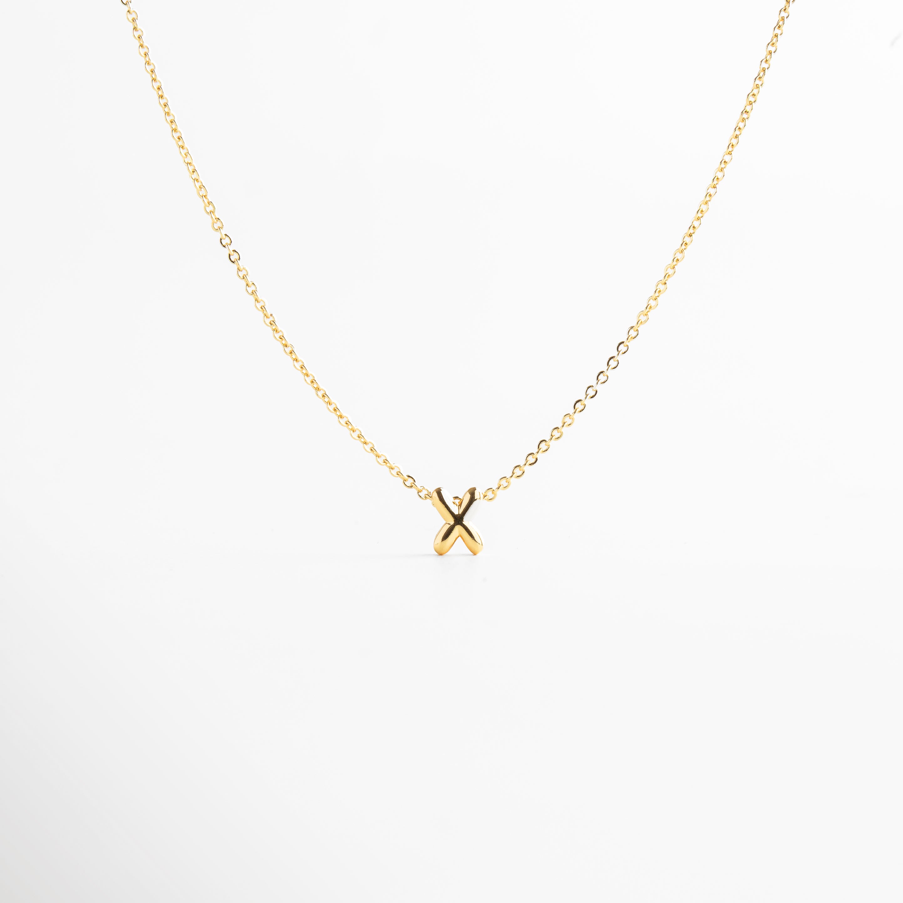 grosor del collar mini con inicial X dorada, detalle del diseño bold en la letra X del collar, cadena fina con dije de inicial X, acabado enchapado en oro 18K con letra X, collar de cobre con recubrimiento dorado