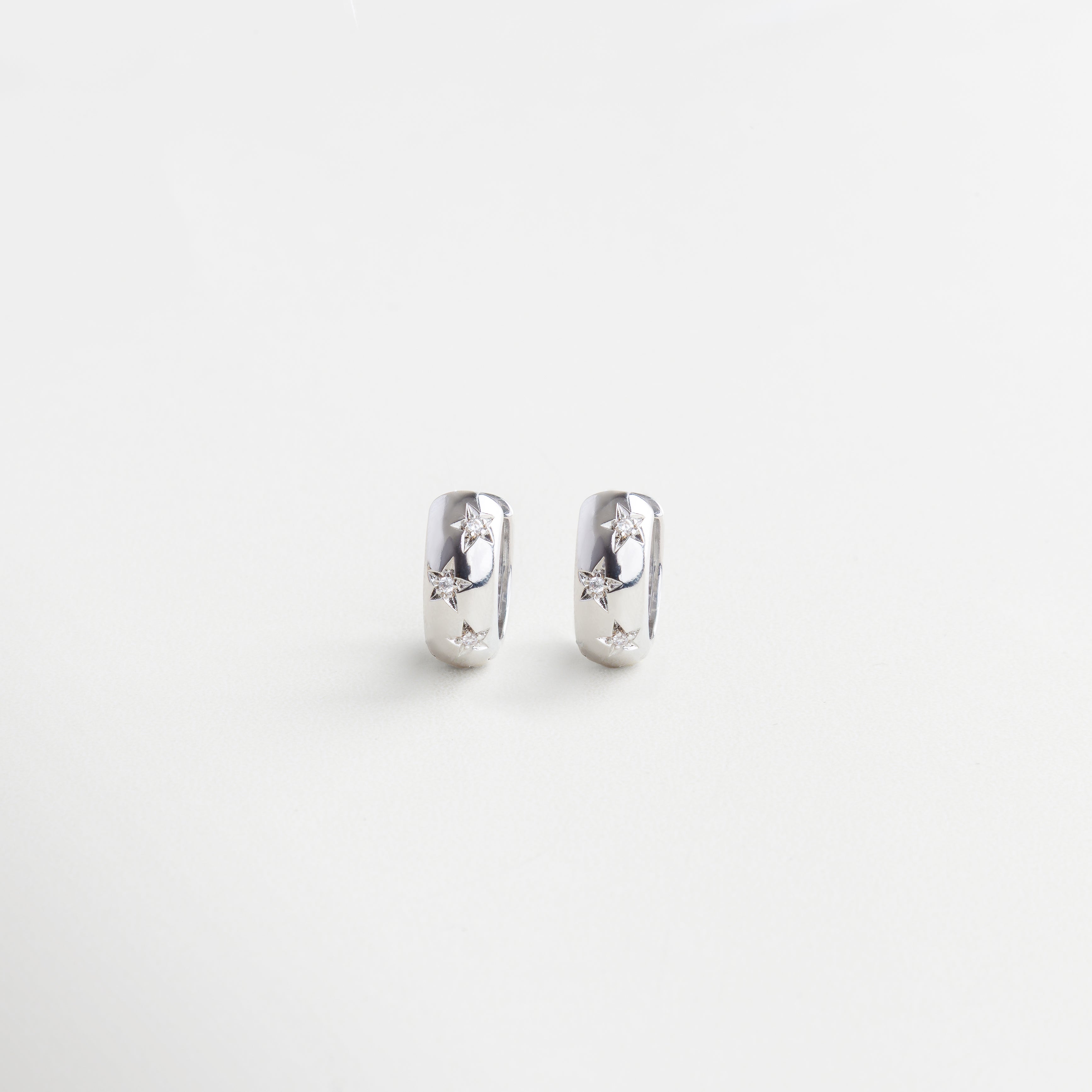 Arracadas plateadas con estrellas y zirconias, Aretes de aro con diseño celestial, Hoops con acabado en oro blanco 18K, Aretes pequeños estilo constelación plateada, Par de aros con estrellas brillantes