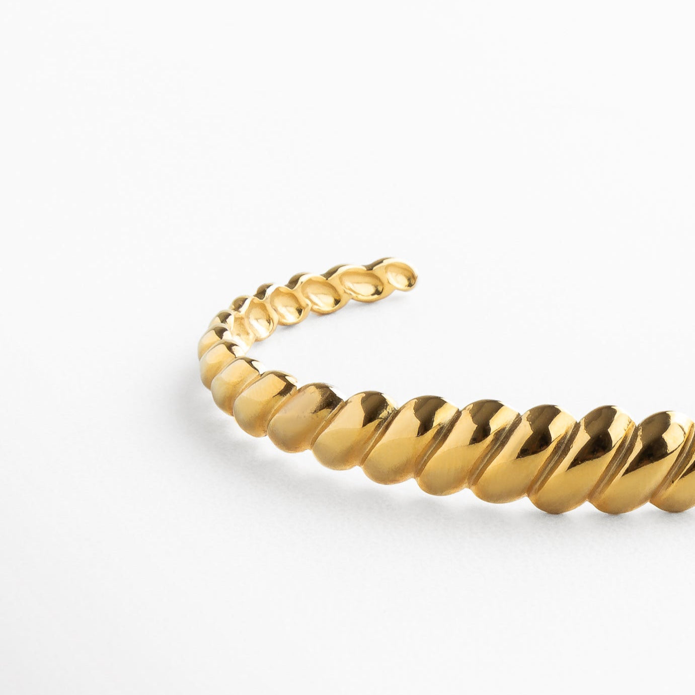 Pulsera dorada vista en ángulo con líneas diagonales elegantes, Perfil estructurado de brazalete dorado con diseño grabado, Contraste de luz y sombra en textura geométrica dorada, Vista angular del diseño contemporáneo en dorado