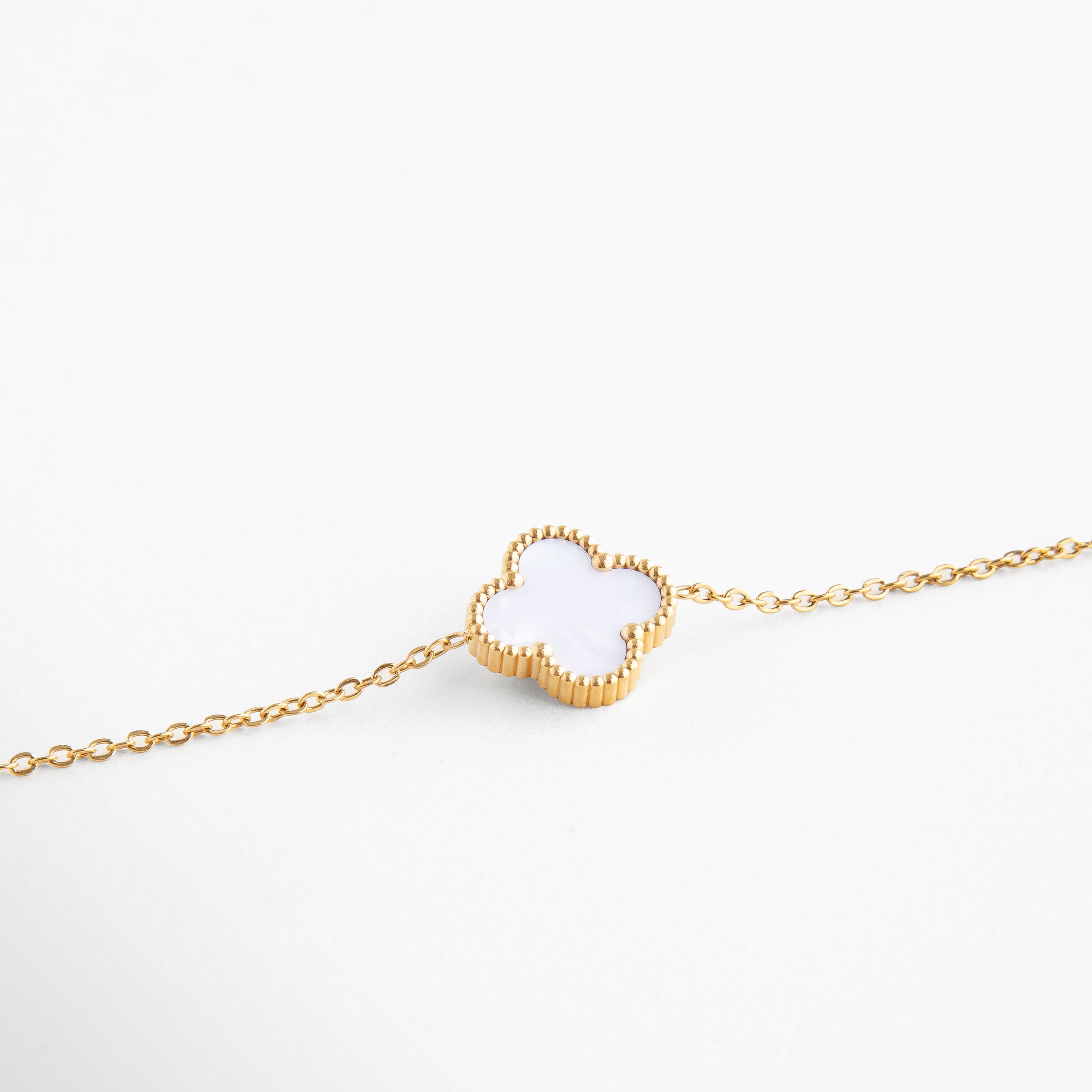 Trébol blanco con incrustación de nácar brillante, Contorno dorado suave que enmarca el dije central, Superficie lisa del nácar con reflejo perlado, Acabado pulido que resalta el diseño delicado, Unión precisa entre cadena y charm de trébol