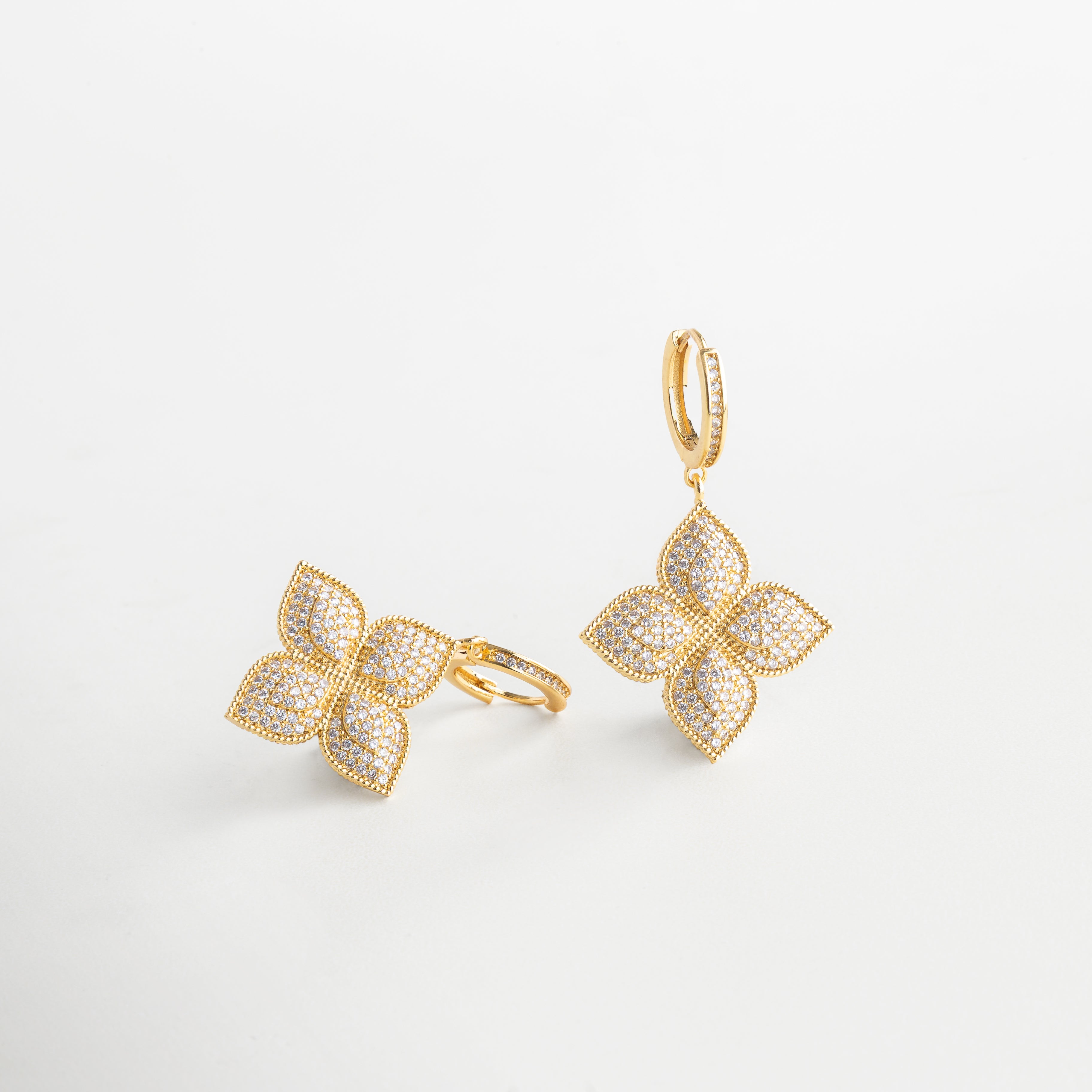 Vista lateral de aretes florales dorados con volumen, Aretes de flor con diseño tridimensional y brillo en ángulo, Aretes con forma de flor vistos de lado, diseño estructurado, Silueta floral dorada con incrustaciones de zirconias