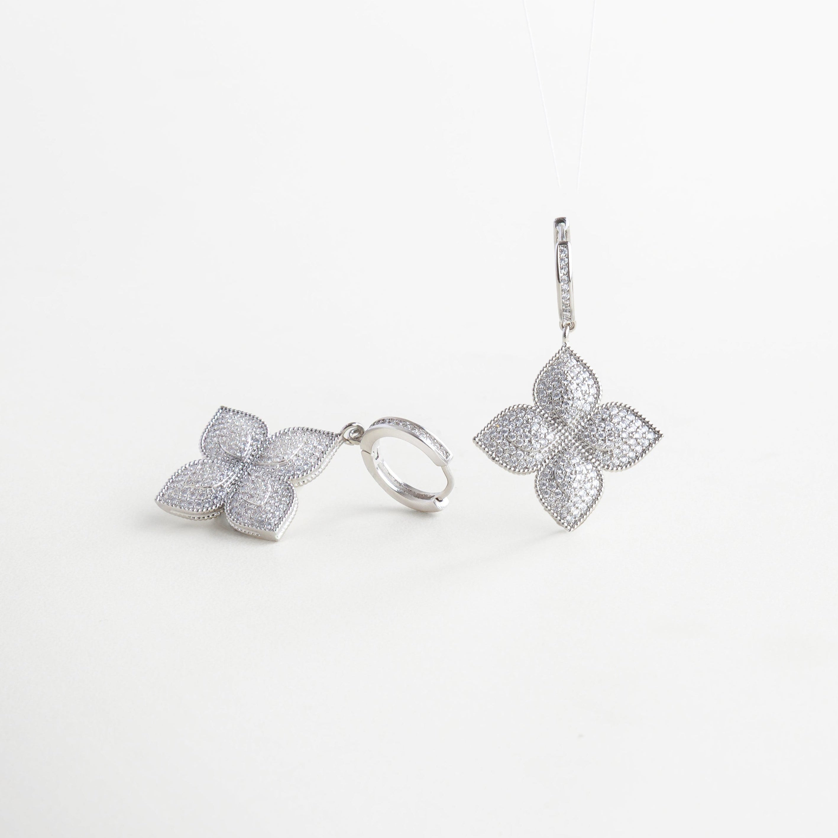 Vista lateral de aretes florales con acabado plateado, Aretes plateados con forma de flor y volumen, Aretes con diseño floral vistos en ángulo, acabado brillante, Silueta floral tridimensional con zirconias en tono plata
