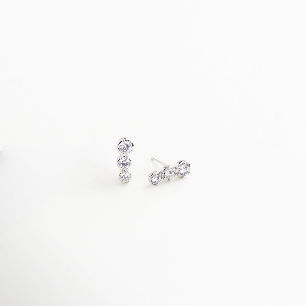 Aretes plateados vistos de lado con diseño de tres esferas, Diseño lateral de aretes pequeños con zirconias en tono plata, Aretes con forma de triada plateada y brillo delicado, Vista angular de aretes plateados con incrustaciones