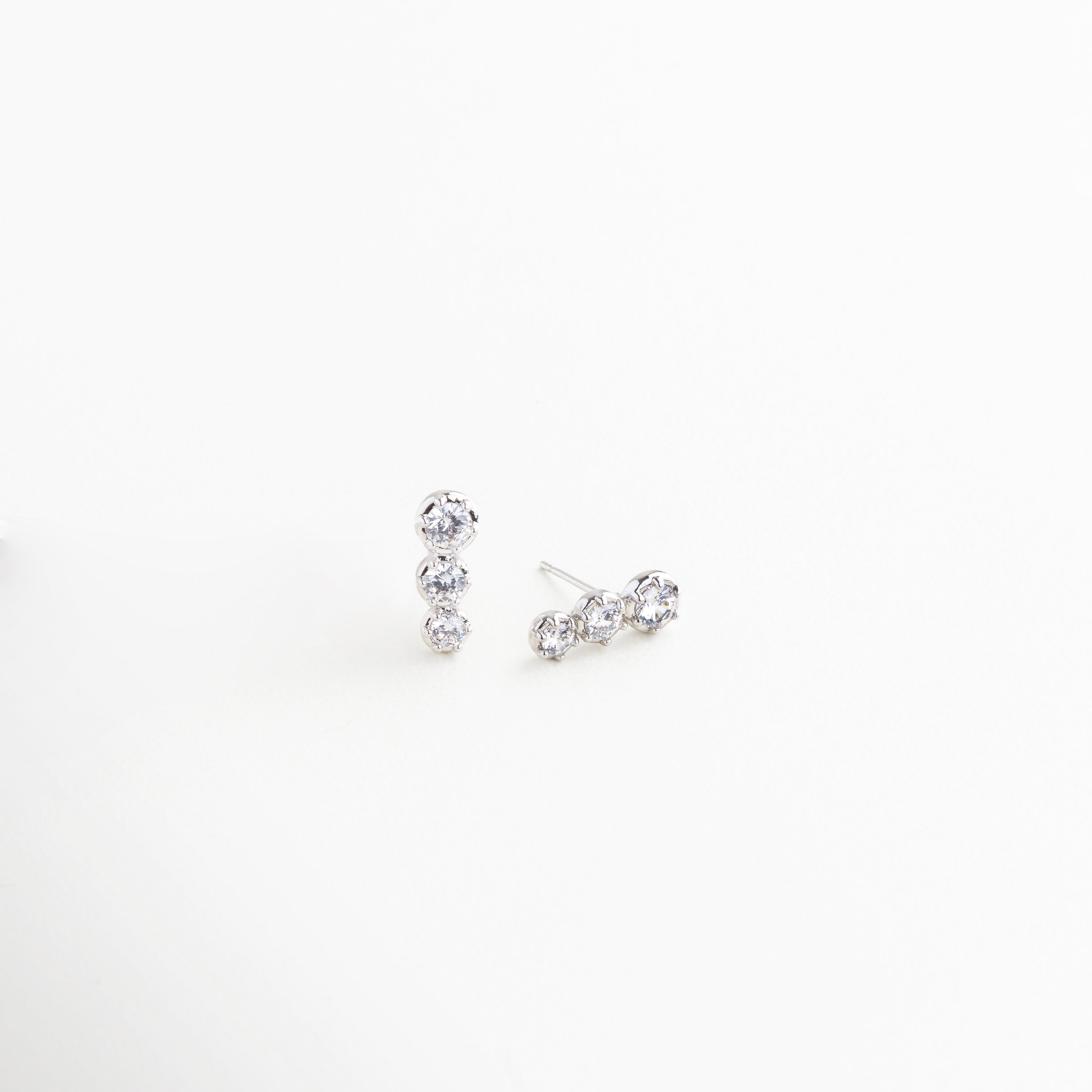Aretes plateados vistos de lado con diseño de tres esferas, Diseño lateral de aretes pequeños con zirconias en tono plata, Aretes con forma de triada plateada y brillo delicado, Vista angular de aretes plateados con incrustaciones