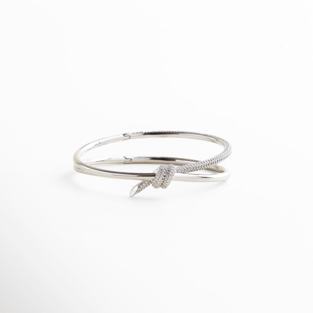 escala real de pulsera rígida plateada con nudo, proporción del nudo central en relación con la pulsera, tamaño visible en muñeca con diseño abierto, dimensión visual del brazalete en uso, forma estructurada y tamaño del diseño rígido