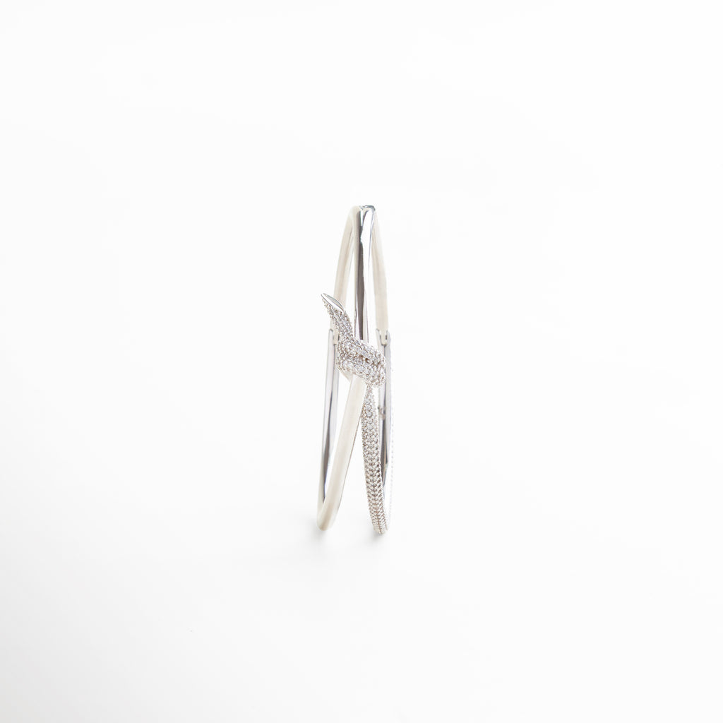 pulsera plateada rígida puesta en la muñeca, cómo luce el nudo con zirconias al usarse, joya plateada combinada en look sofisticado, complemento ideal para looks de día o noche, estilo moderno con brillo elegante en uso