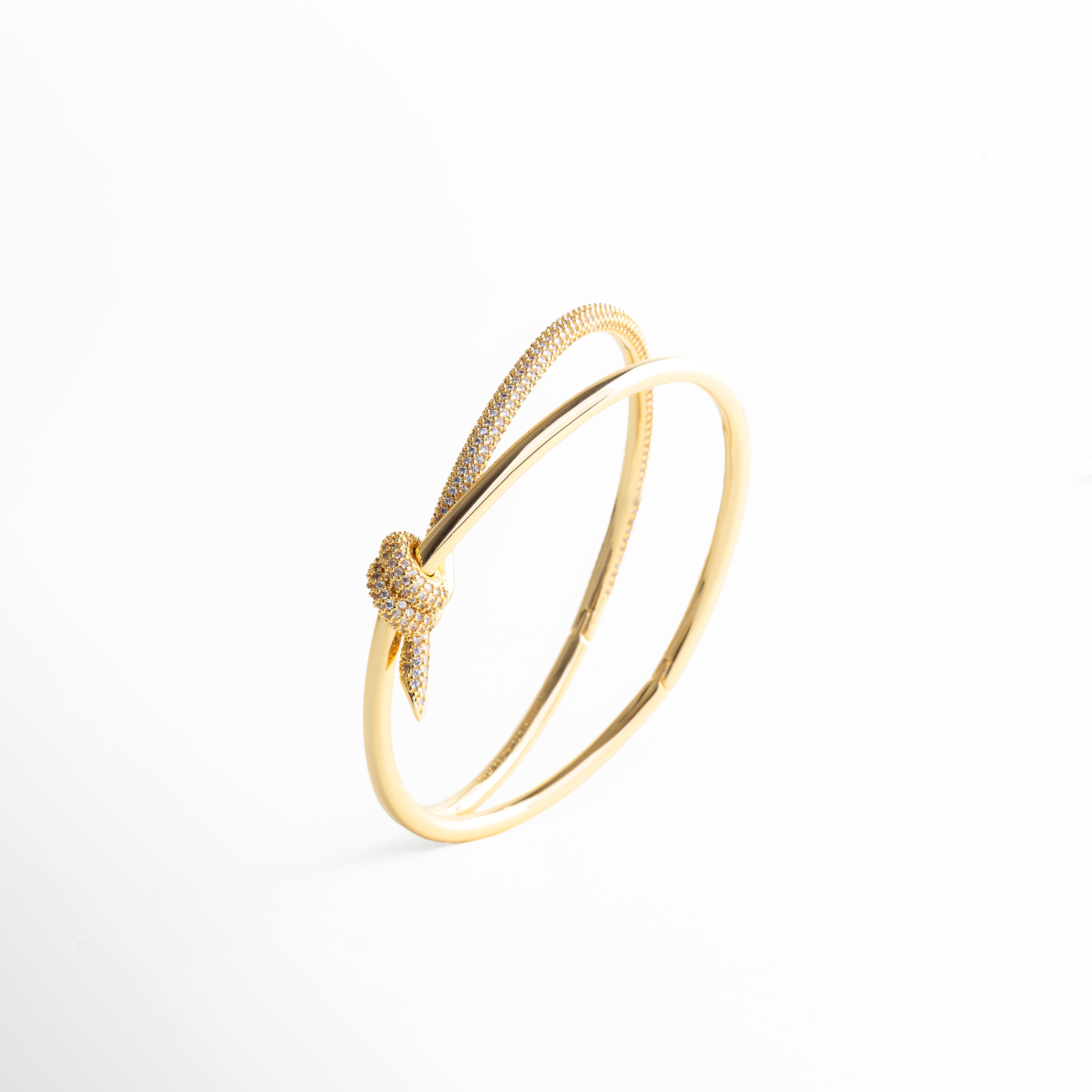 pulsera dorada con detalle, nudo dorado joyería, pulsera con diseño simbólico, joyería elegante mujer, accesorios dorados refinados, pulsera de diseño fino, joyería contemporánea, pulsera sofisticada