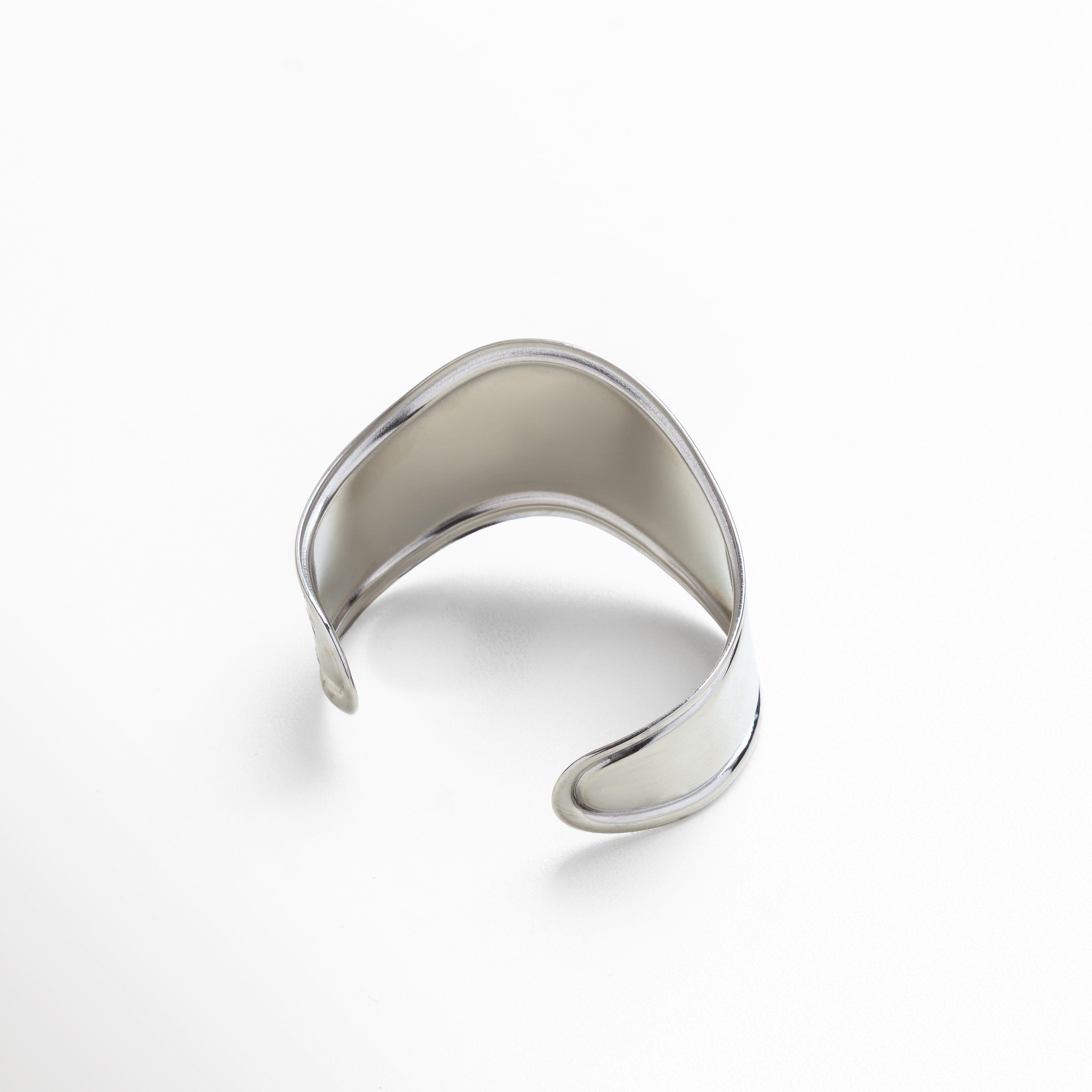 Pulsera plateada bold mostrada sobre mano para referencia, Proporción de ancho y diámetro en muñeca femenina, Tamaño real comparado con superficie neutra, Grosor visible de brazalete rígido en uso, Vista completa de dimensiones 6.8 x 4.1 cm