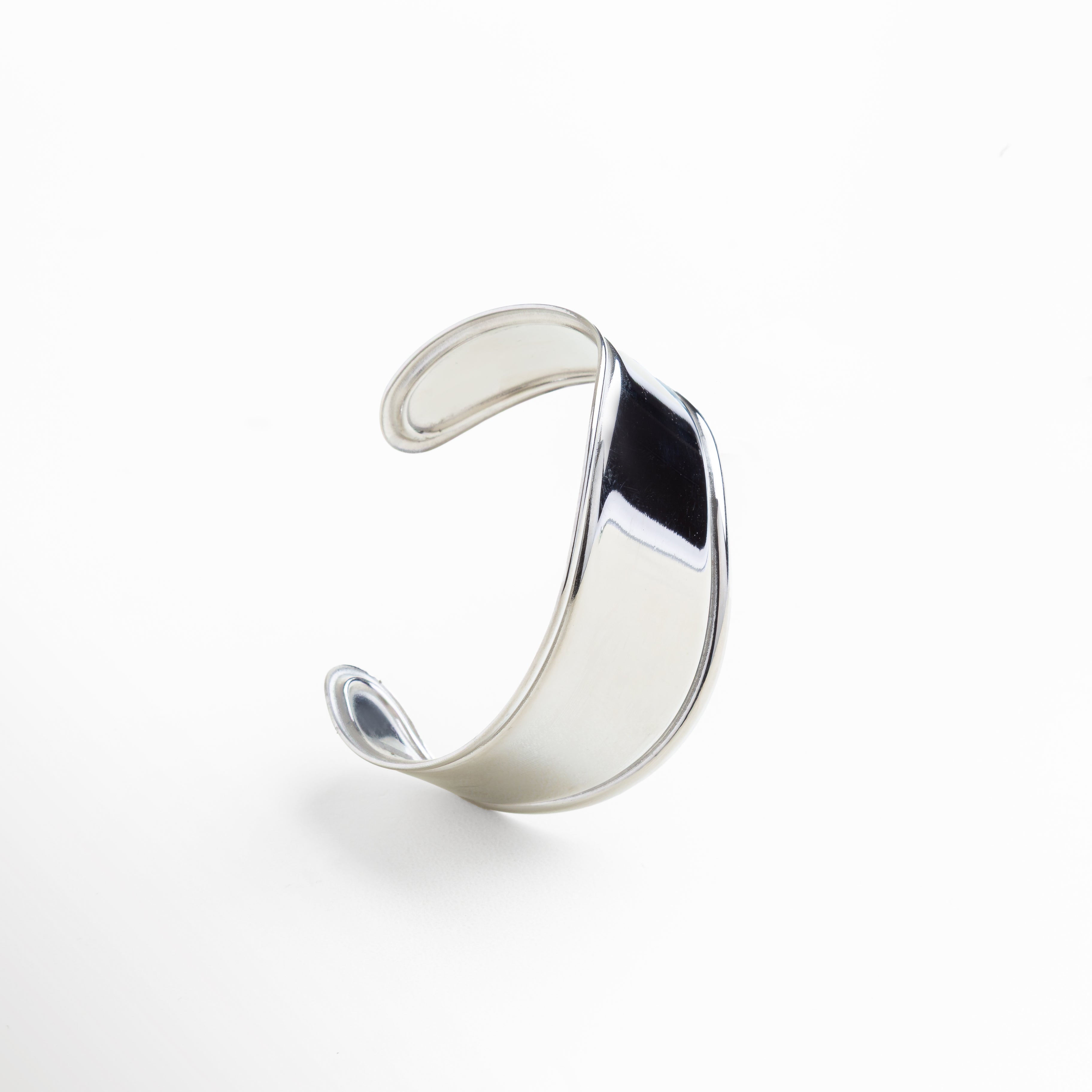 Primer plano de acabado pulido en brazalete plateado, Detalle de superficie lisa y reflectante en pulsera rígida, Textura espejo en acero inoxidable enchapado en oro blanco, Bordes redondeados y suaves del diseño bold, Unión impecable en estructura rígida plateada