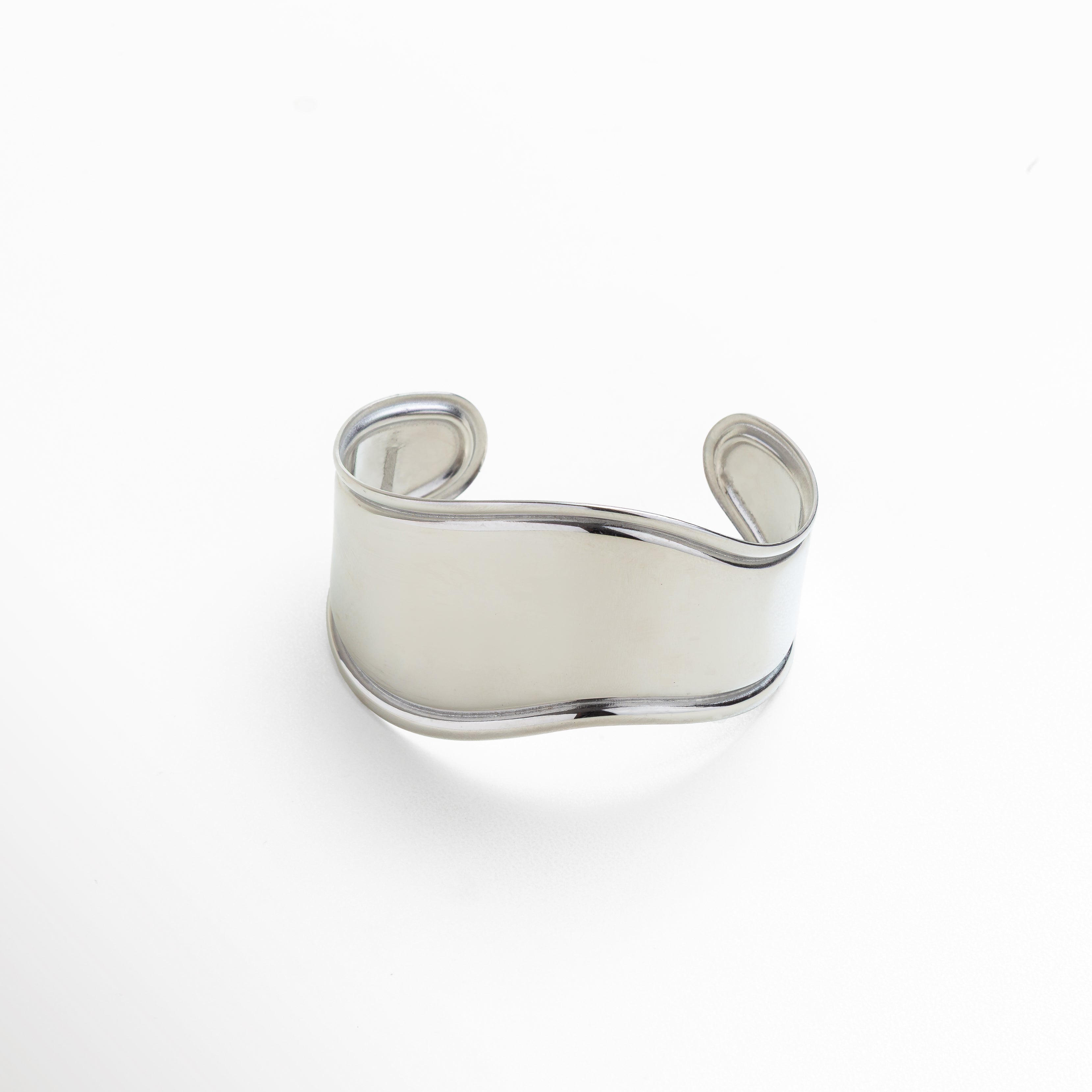 Pulsera rígida plateada diseño bold minimalista, Brazalete plateado ancho con acabado pulido espejo, Joyería moderna en oro blanco 18K estilo audaz, Pulsera plateada elegante de líneas fluidas, Accesorio statement minimalista en tono plateado
