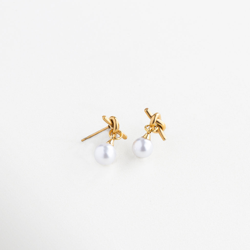 Diseño de nudo dorado con perla colgante, Aretes con forma entrelazada y perla brillante, Aretes de acero inoxidable con perla sintética y giro moderno, Vista lateral de aretes Knotté con estructura elegante