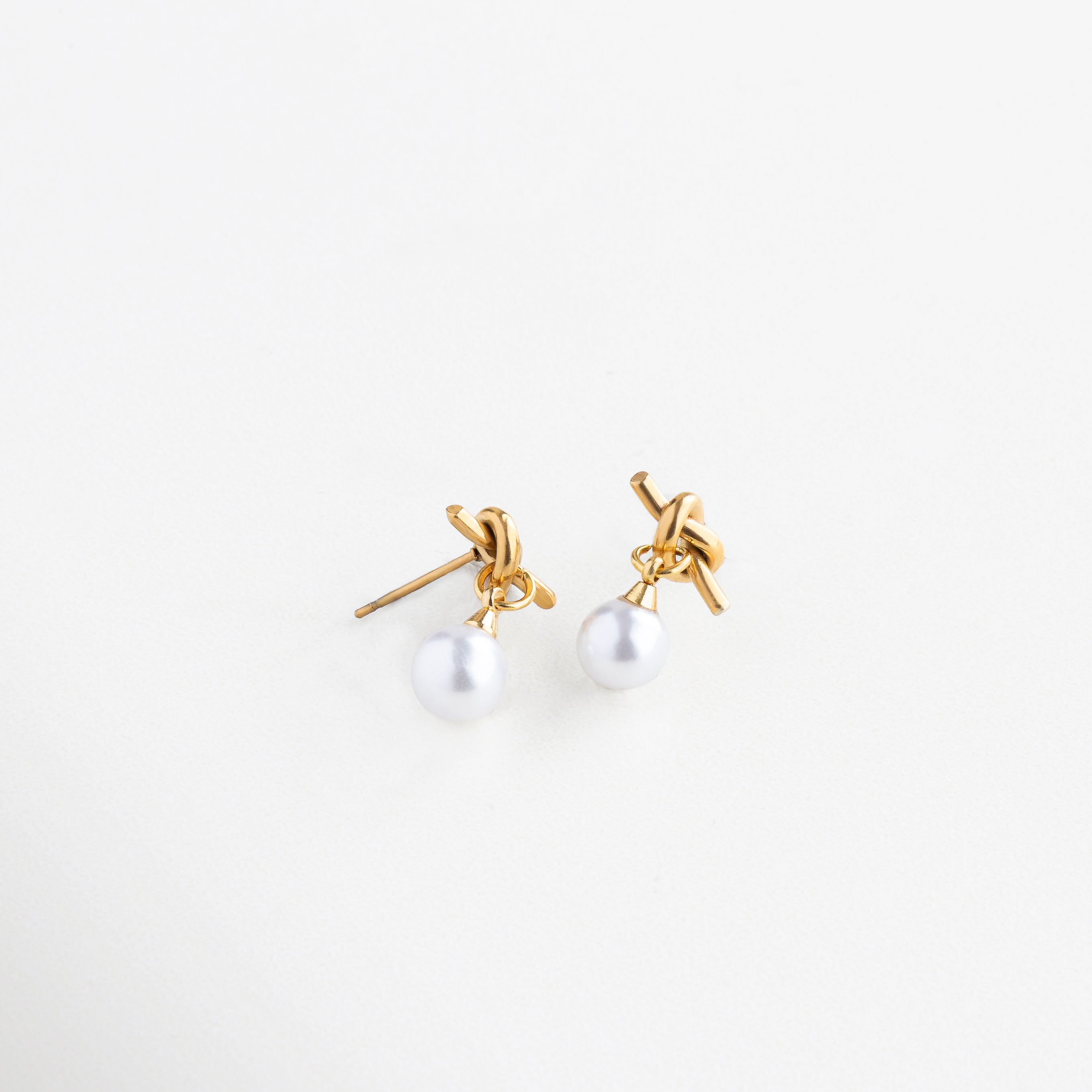 Diseño de nudo dorado con perla colgante, Aretes con forma entrelazada y perla brillante, Aretes de acero inoxidable con perla sintética y giro moderno, Vista lateral de aretes Knotté con estructura elegante