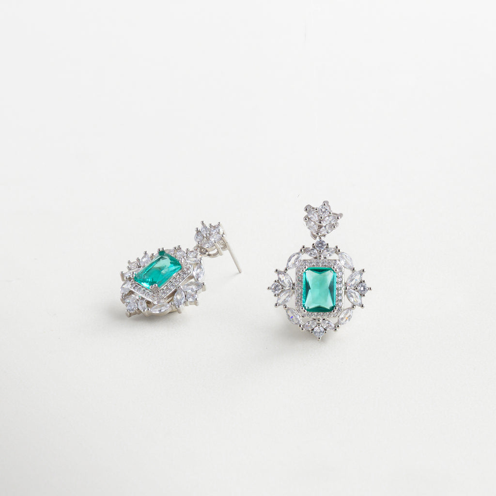 Aretes con forma floral y piedra verde vistos en ángulo, Diseño lateral de aretes con centro verde y zirconias brillantes, Vista en ángulo de aretes con piedra esmeralda sintética y detalles brillantes, Aretes Sami Mint desde vista lateral, con forma delicada y femenina