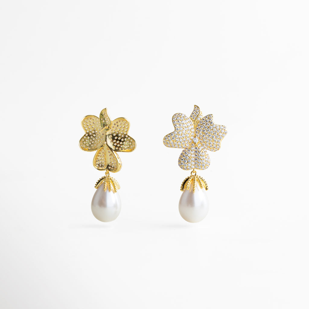 Aretes dorados con forma de hoja y perla colgante, diseño elegante tipo statement con brillo y caída sofisticada.