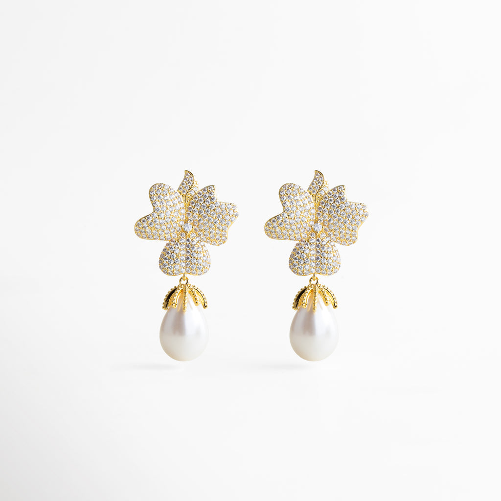 Par de aretes dorados con forma de flor y perla blanca colgante, diseño glamuroso y femenino que combina brillo y elegancia atemporal.