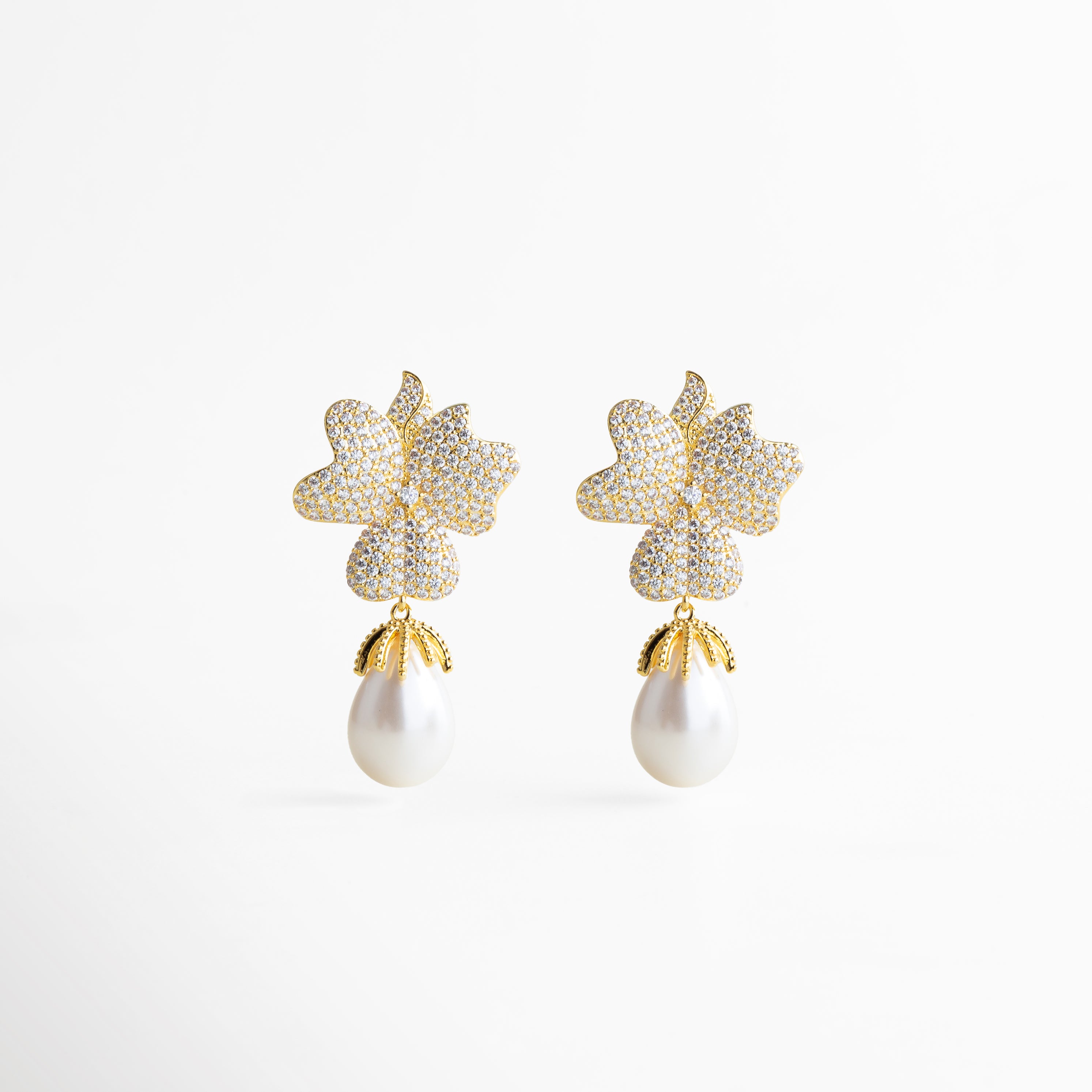 Par de aretes dorados con forma de flor y perla blanca colgante, diseño glamuroso y femenino que combina brillo y elegancia atemporal.