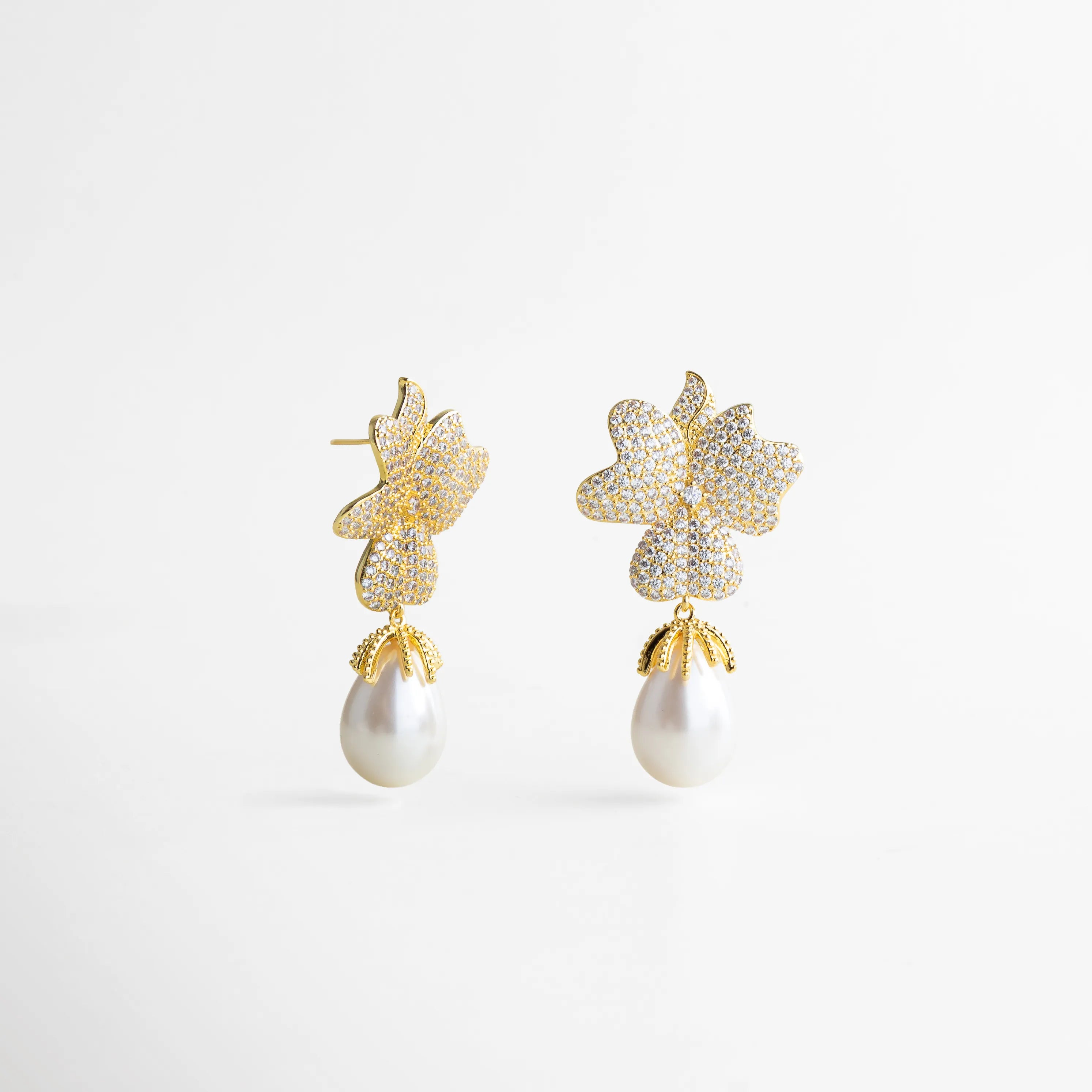 Aretes dorados con forma de flor doble cubierta de zirconias, acompañados de una elegante perla blanca colgante en forma de gota.