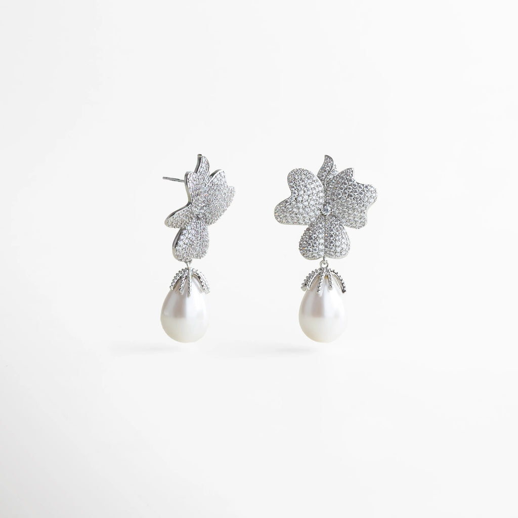 Aretes plateados con forma de flor doble cubierta de zirconias, acompañados de una elegante perla blanca colgante en forma de gota.