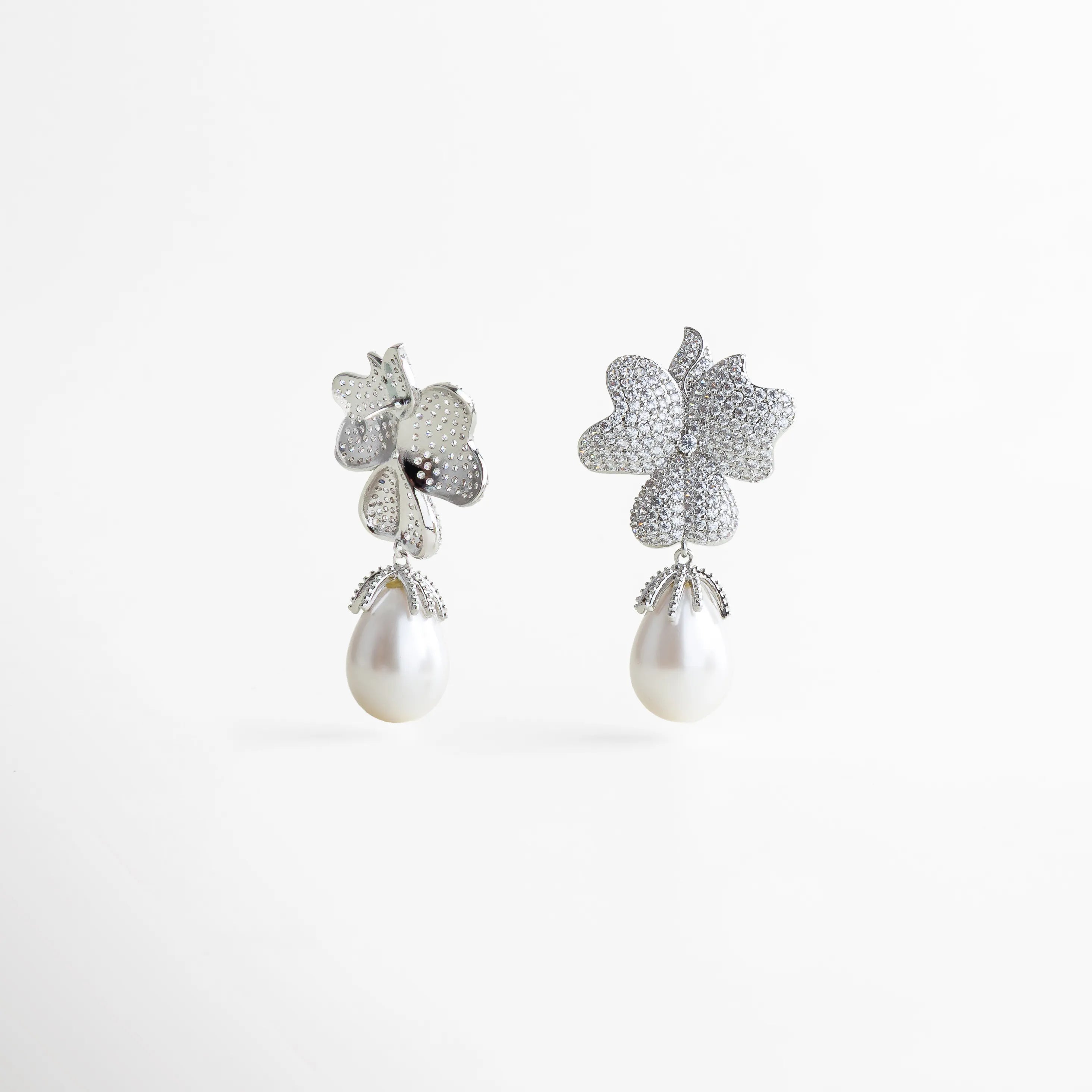 Aretes plateados de flor doble con incrustaciones brillantes y perlas blancas colgantes, diseño sofisticado con acabado reluciente y detalles en relieve.