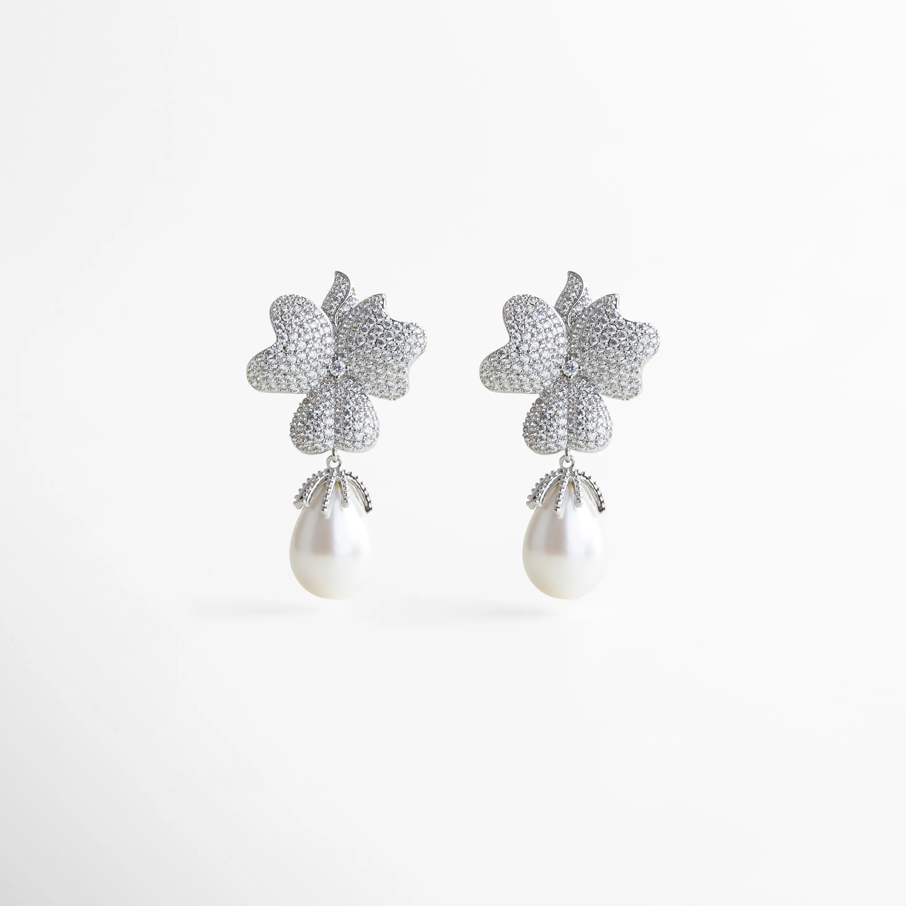 Par de aretes plateados con forma de flor y perla blanca colgante, diseño glamuroso y femenino que combina brillo y elegancia atemporal.