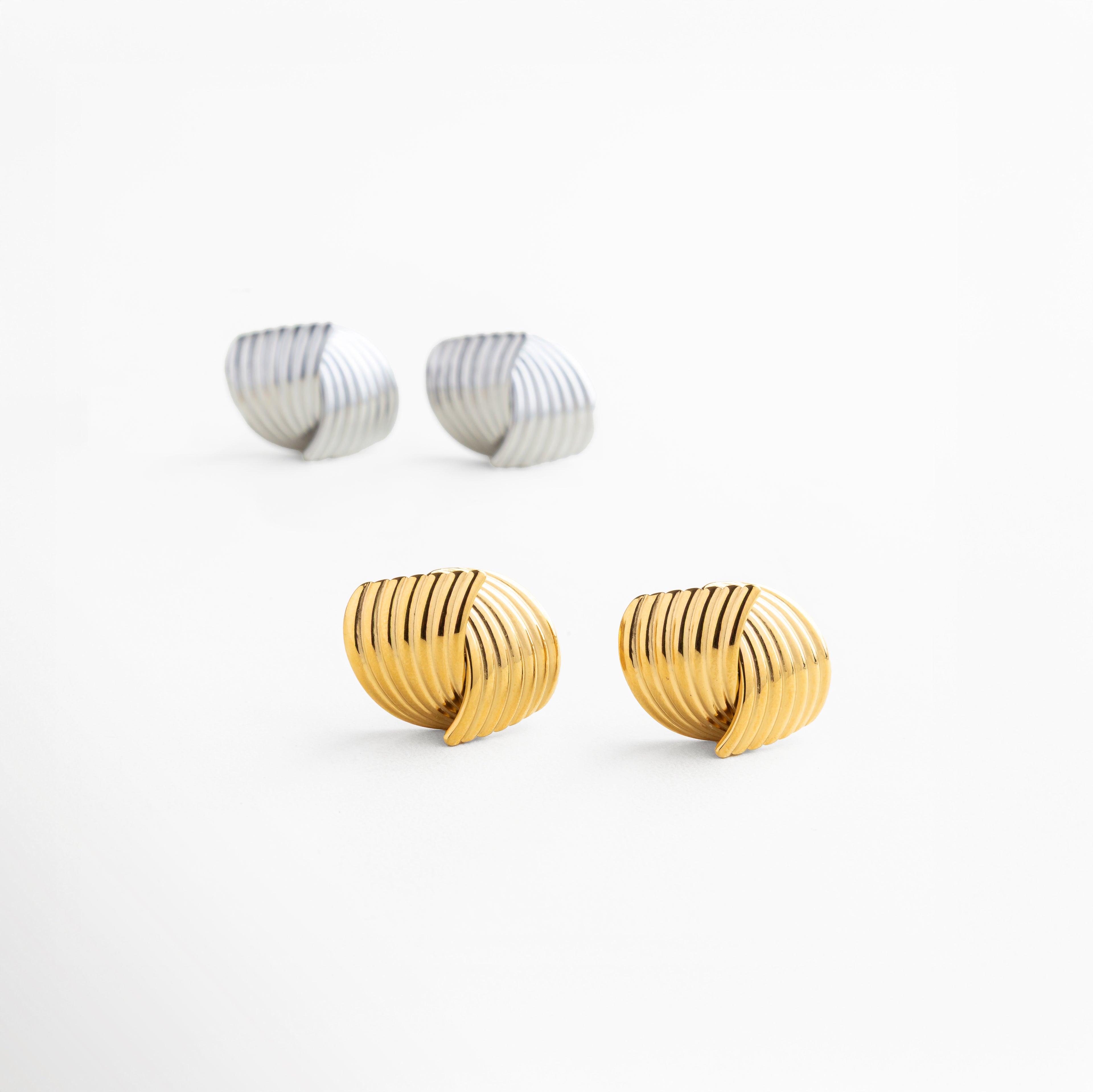 Aretes Ita Golden en acero inoxidable 316 con oro 18K, longitud 2.5 cm y ancho 2.1 cm, escala real para referencia de tamaño, diseño entrelazado versátil para looks casuales o elegantes
