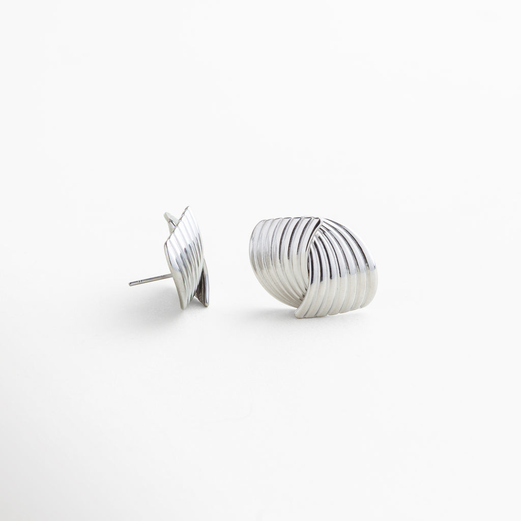 Detalle de textura en aretes Ita Silver de acero inoxidable 316, acabado enchapado en oro blanco 18K con superficie texturizada, diseño fluido y envolvente que aporta elegancia y fuerza, piezas de joyería versátiles y de lujo accesible