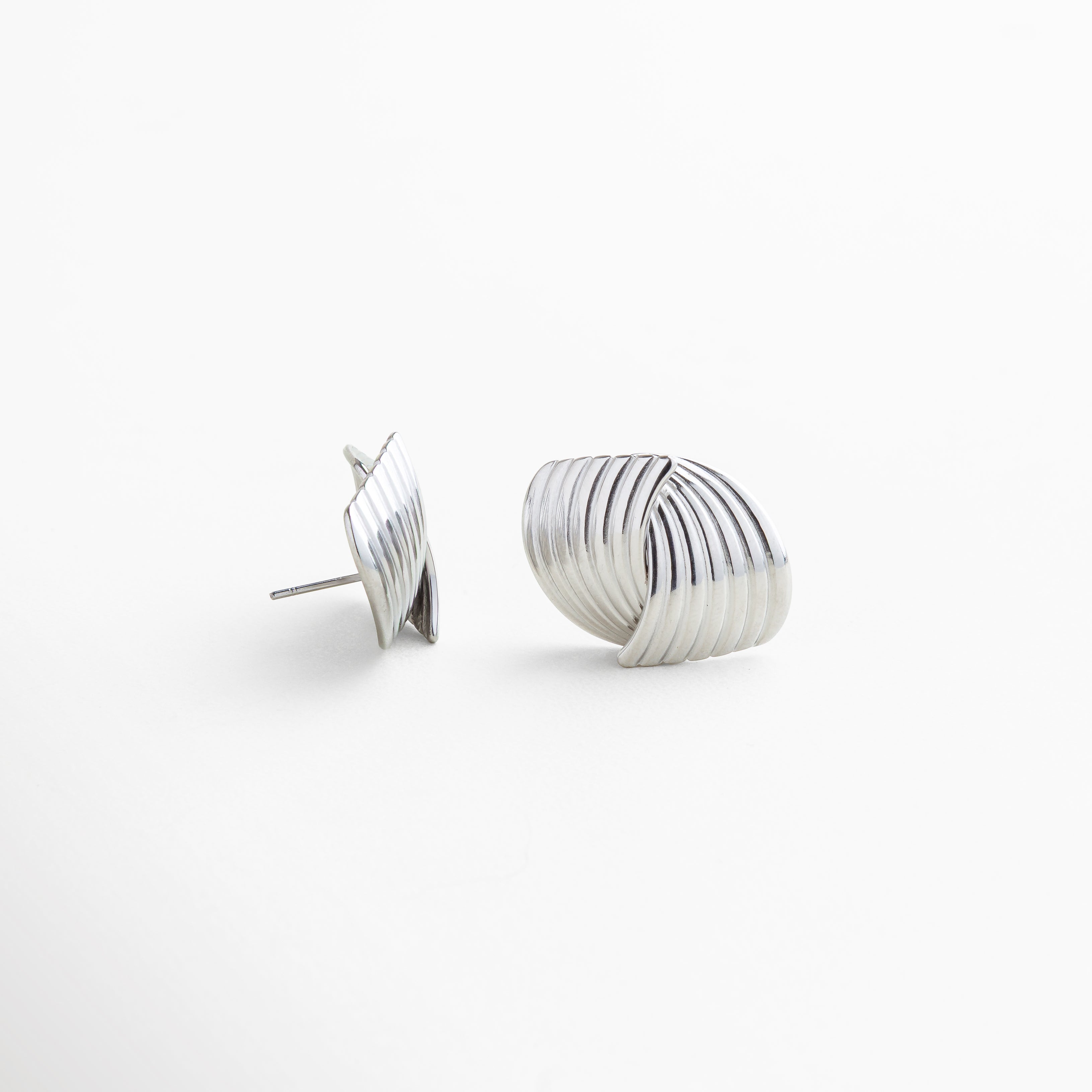 Detalle de textura en aretes Ita Silver de acero inoxidable 316, acabado enchapado en oro blanco 18K con superficie texturizada, diseño fluido y envolvente que aporta elegancia y fuerza, piezas de joyería versátiles y de lujo accesible