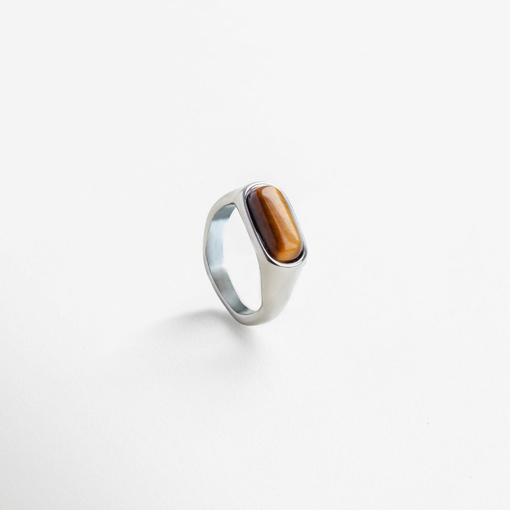 Anillo dorado con piedra natural visto de perfil, Diseño elegante con piedra ojo de tigre desde un lateral, Corte rectangular de la piedra desde un ángulo moderno, Estructura del anillo en dorado con piedra terrosa