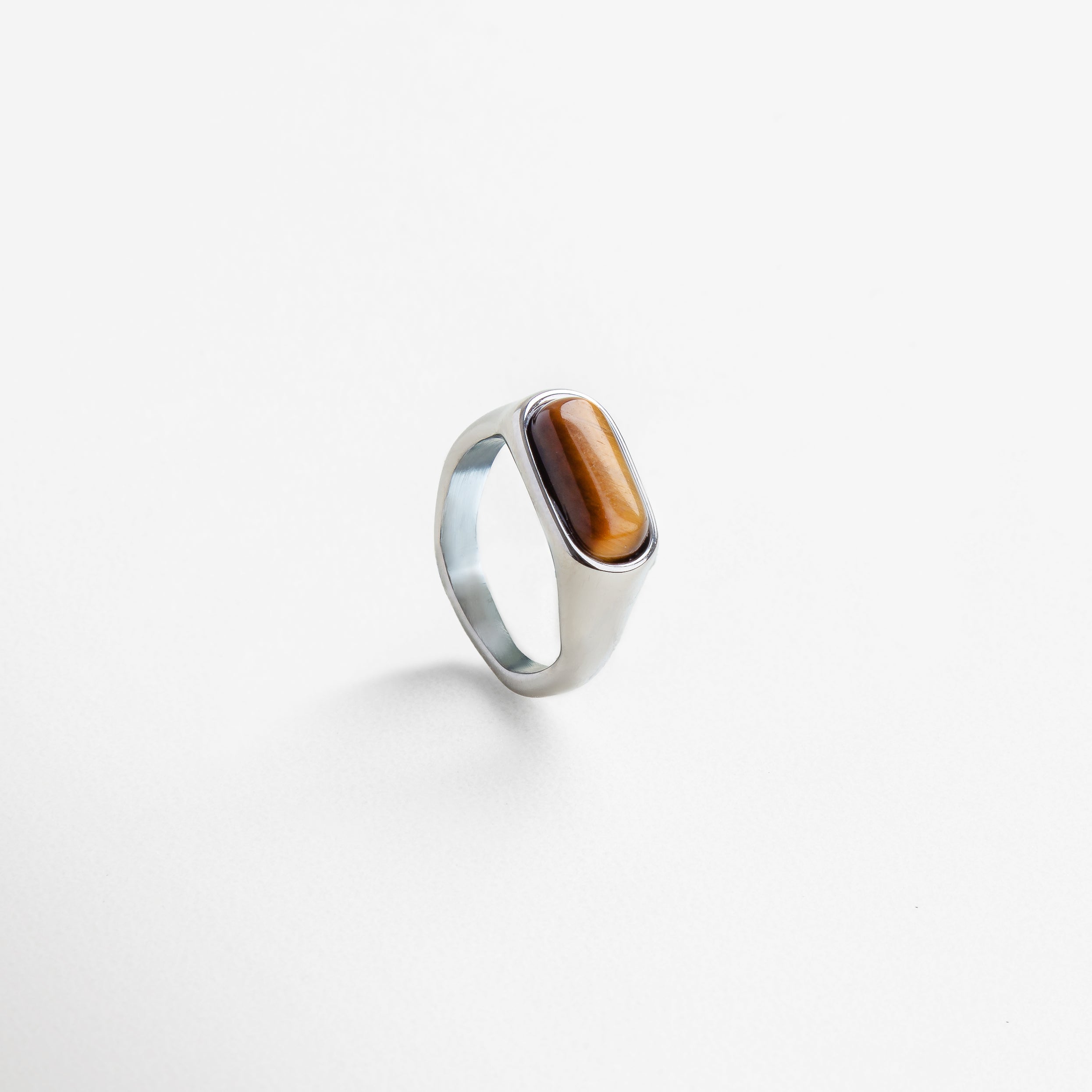 Anillo dorado con piedra natural visto de perfil, Diseño elegante con piedra ojo de tigre desde un lateral, Corte rectangular de la piedra desde un ángulo moderno, Estructura del anillo en dorado con piedra terrosa