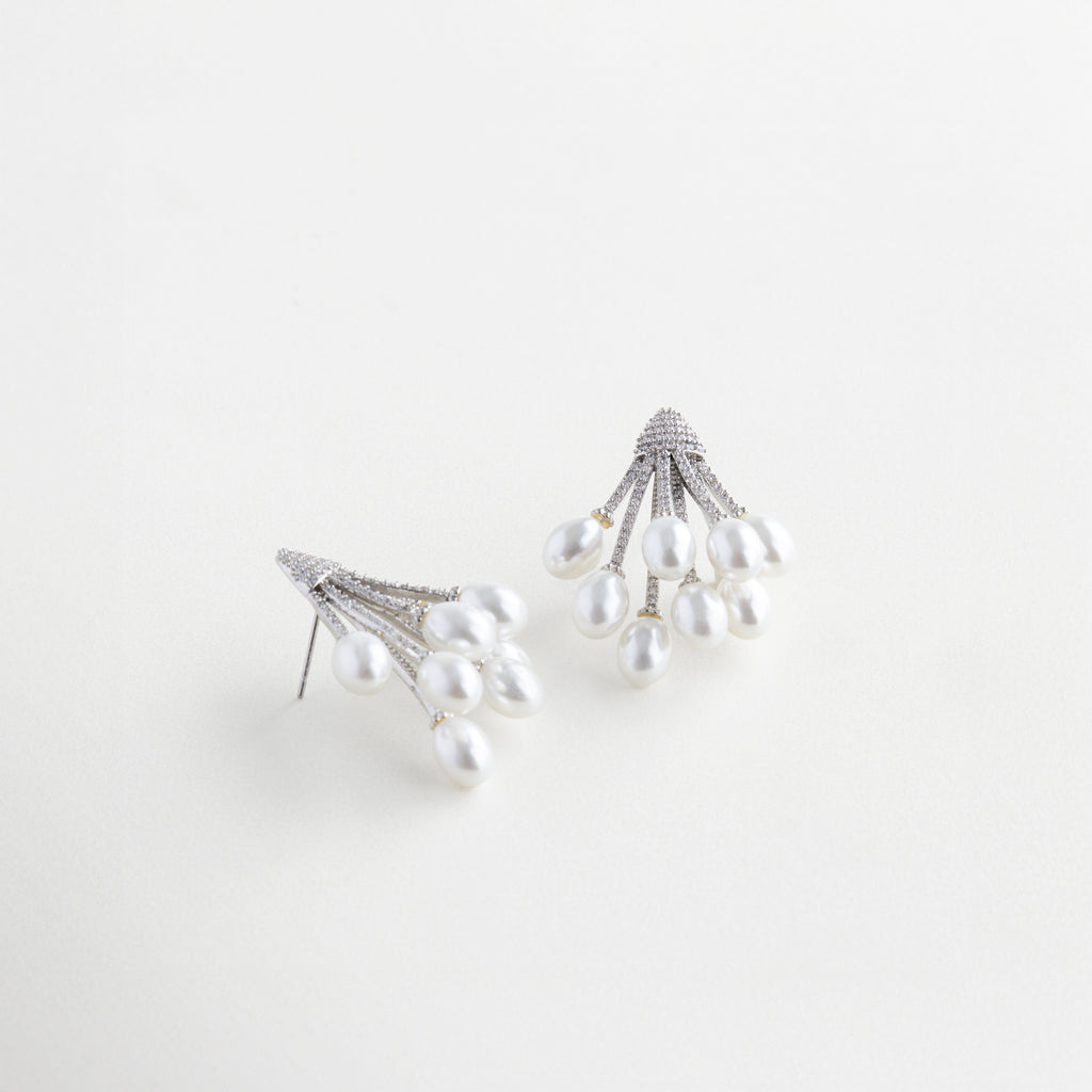 Vista lateral de aretes con perla y zirconias brillantes, Aretes con diseño curvo y perla sintética vistos en ángulo, Joyería elegante con perla en movimiento y toques brillantes, Diseño lateral de aretes con perla suspendida