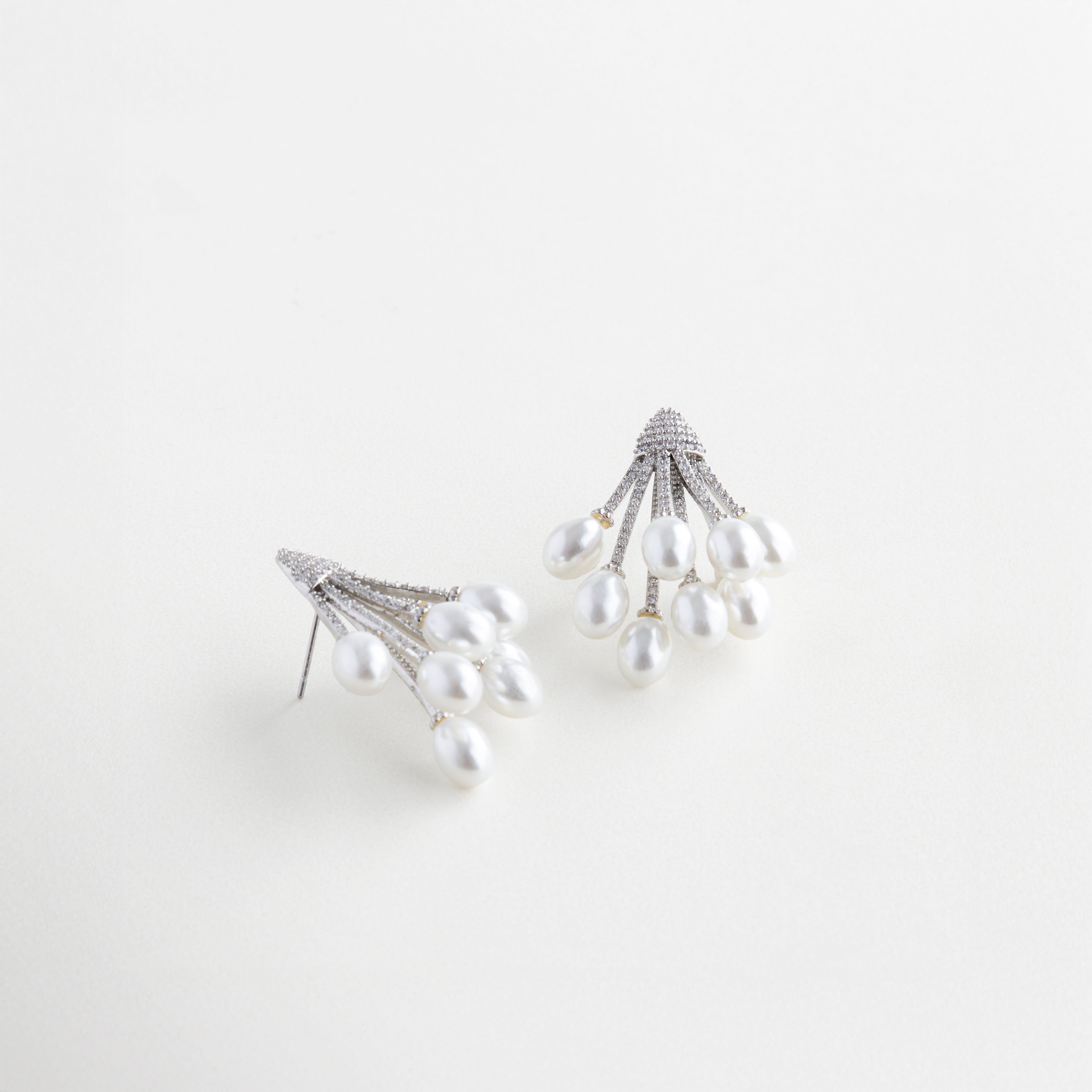 Vista lateral de aretes con perla y zirconias brillantes, Aretes con diseño curvo y perla sintética vistos en ángulo, Joyería elegante con perla en movimiento y toques brillantes, Diseño lateral de aretes con perla suspendida