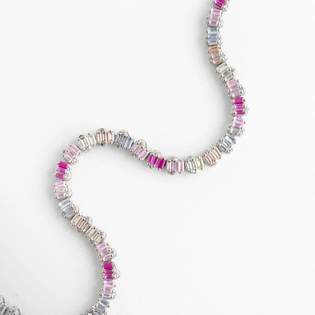 Pulsera flexible de plata con patrón de colores degradados mostrando su diseño fluido, Brazalete de oro blanco y plata 925 con cristales rectangulares en tonos rosados, Pulsera con movimiento "snake" resaltando el brillo de las circonias de colores, Diseño de joyería contemporánea: pulsera de banda delgada con piedras baguette multicolor, Vista de la caída natural de la pulsera plateada con destellos de circonia fucsia.