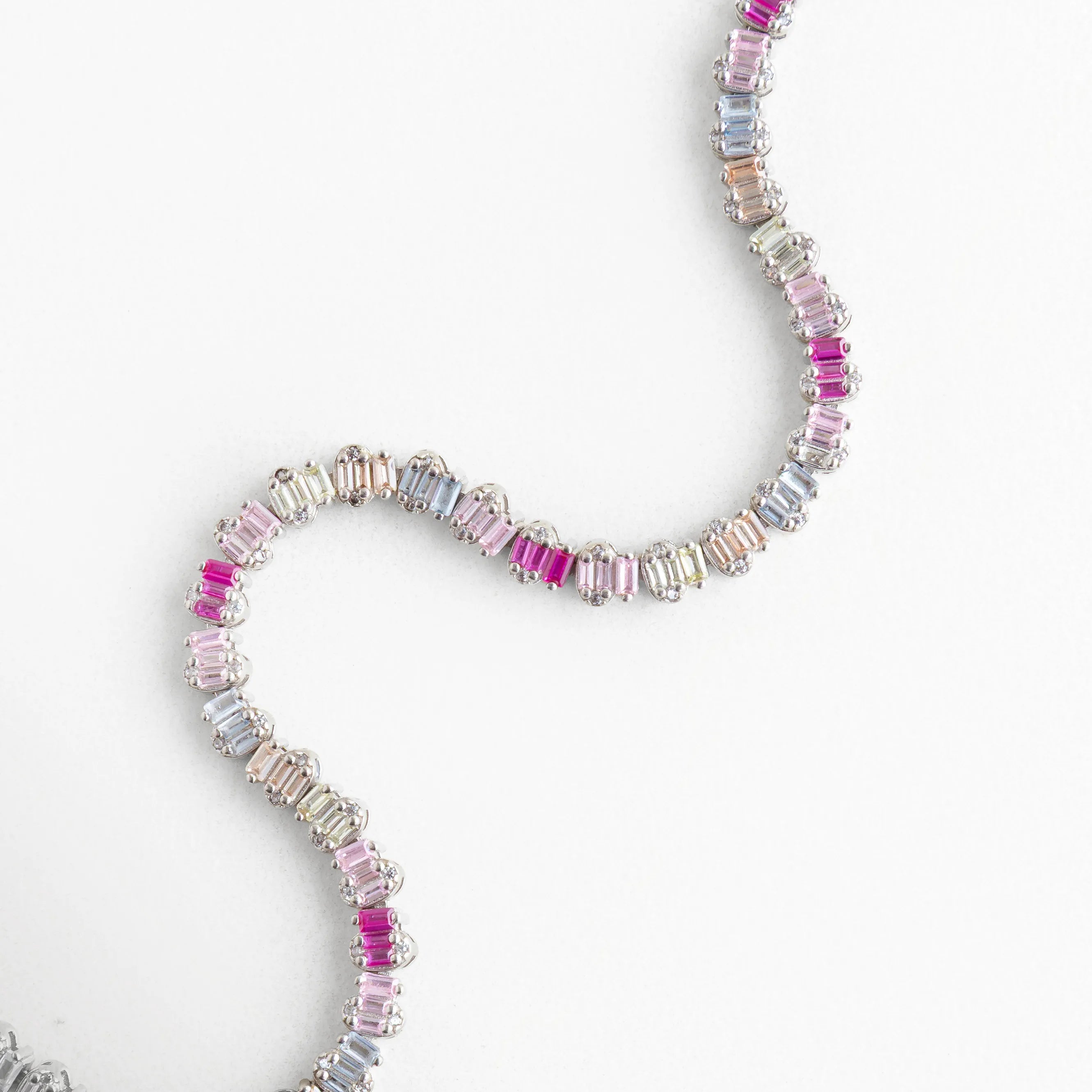 Pulsera flexible de plata con patrón de colores degradados mostrando su diseño fluido, Brazalete de oro blanco y plata 925 con cristales rectangulares en tonos rosados, Pulsera con movimiento "snake" resaltando el brillo de las circonias de colores, Diseño de joyería contemporánea: pulsera de banda delgada con piedras baguette multicolor, Vista de la caída natural de la pulsera plateada con destellos de circonia fucsia.