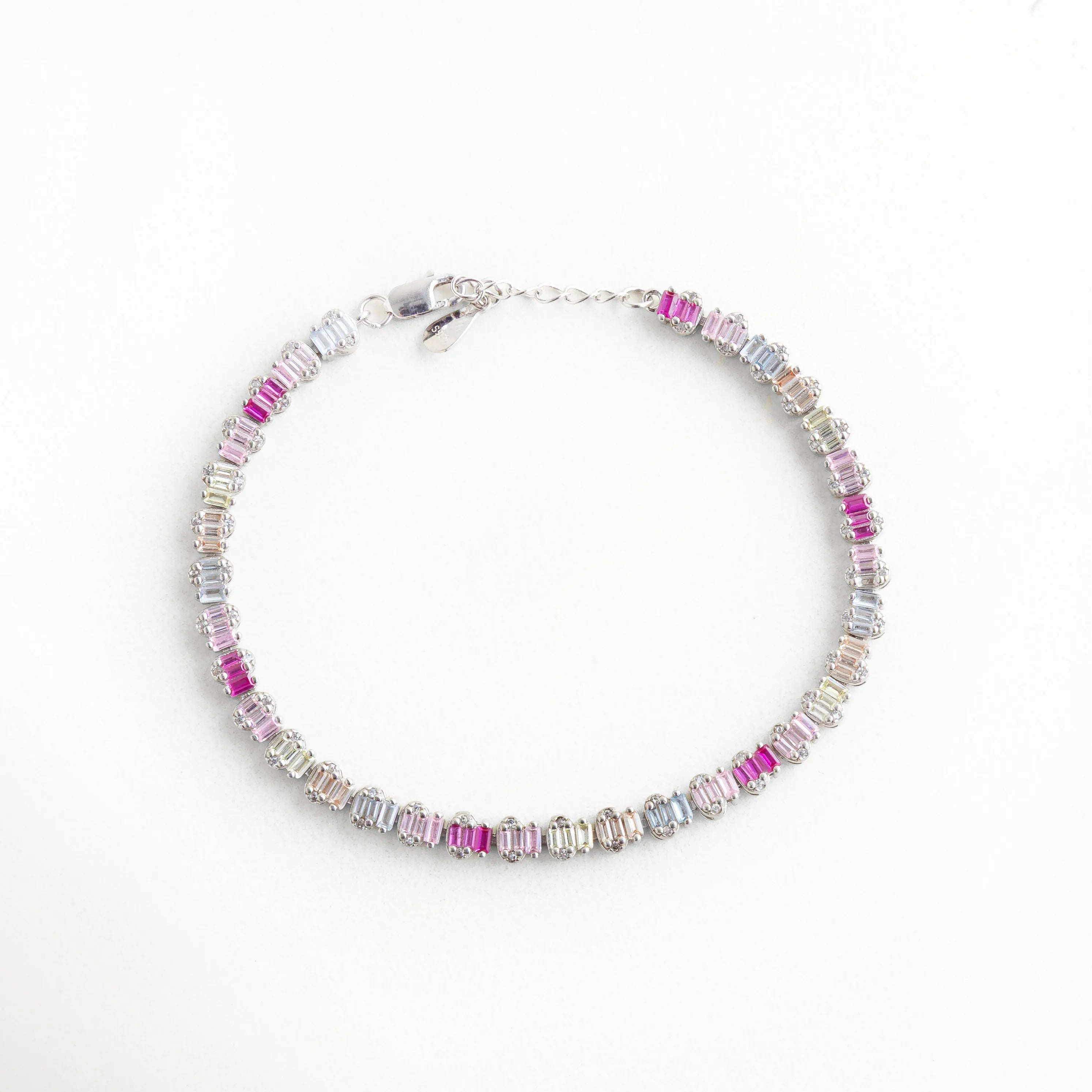 Composición circular de pulsera de plata 925 con baño de oro blanco y piedras de colores, Pulsera completa tipo eternidad con circonias baguette en transición de color fucsia a lila, Brazalete plateado de diseño continuo con cristales brillantes para mujer, Accesorio de muñeca en plata de ley con acabado premium y cristales rectangulares, Vista aérea de pulsera multicolor en oro blanco, ideal para stacking de joyas.